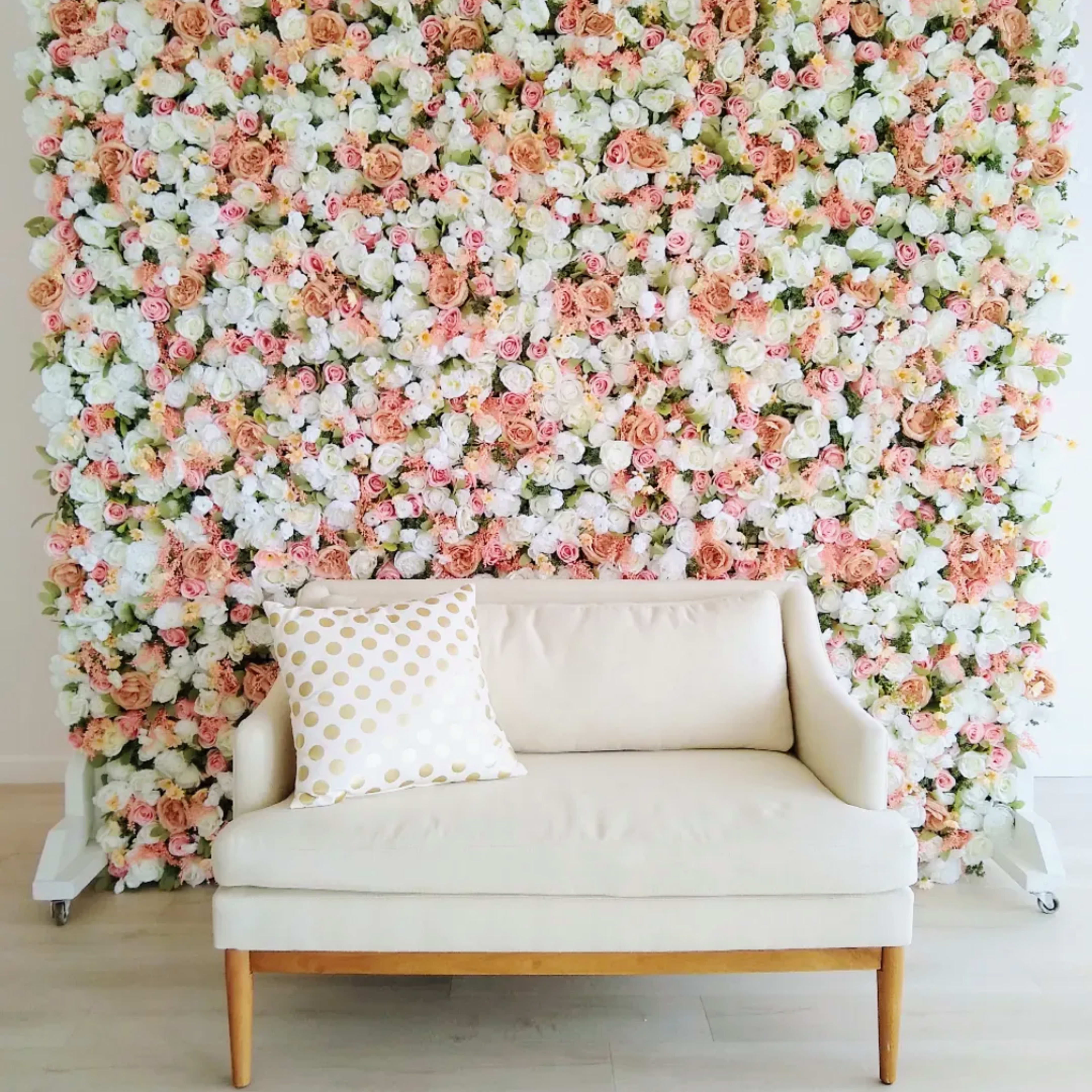 A beige sofa with wooden legs is positioned in front of a backdrop of pink and white floral decorations.