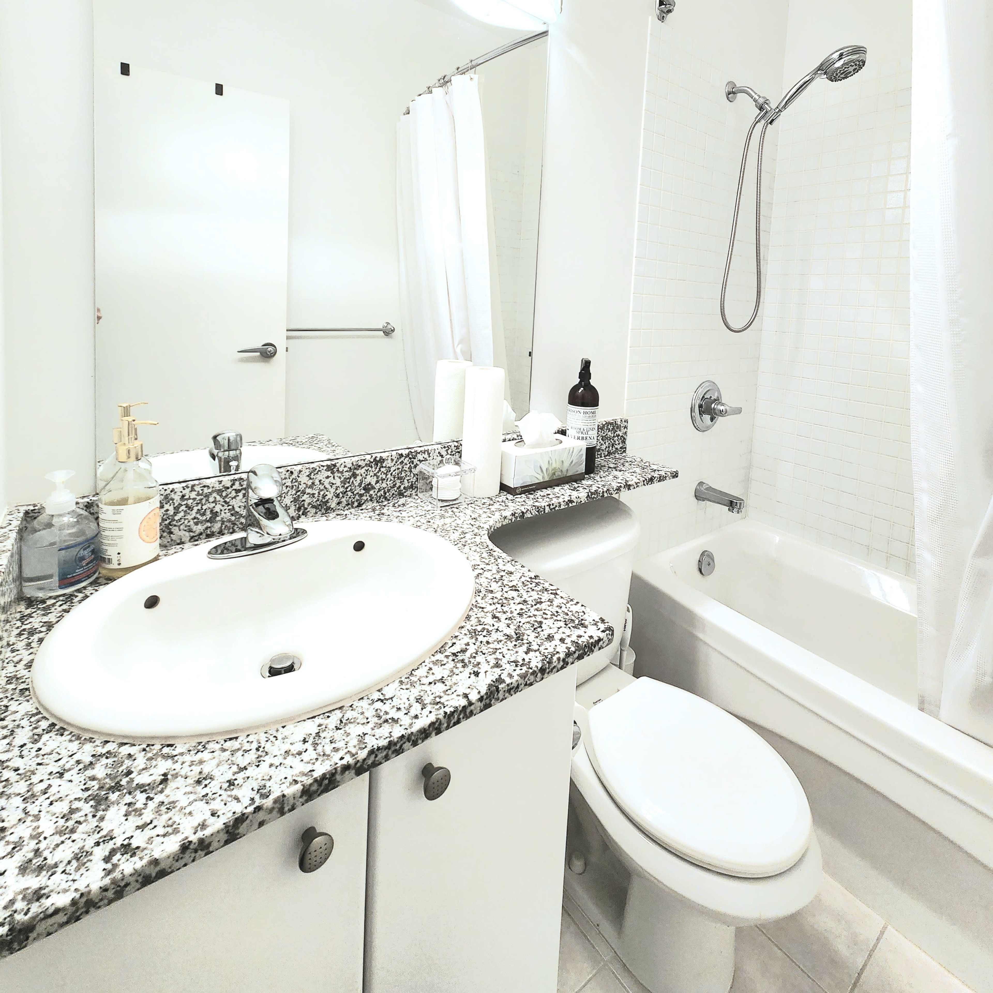 A clean bathroom with a granite countertop, a sink, a bathtub with a shower, and white cabinetry.