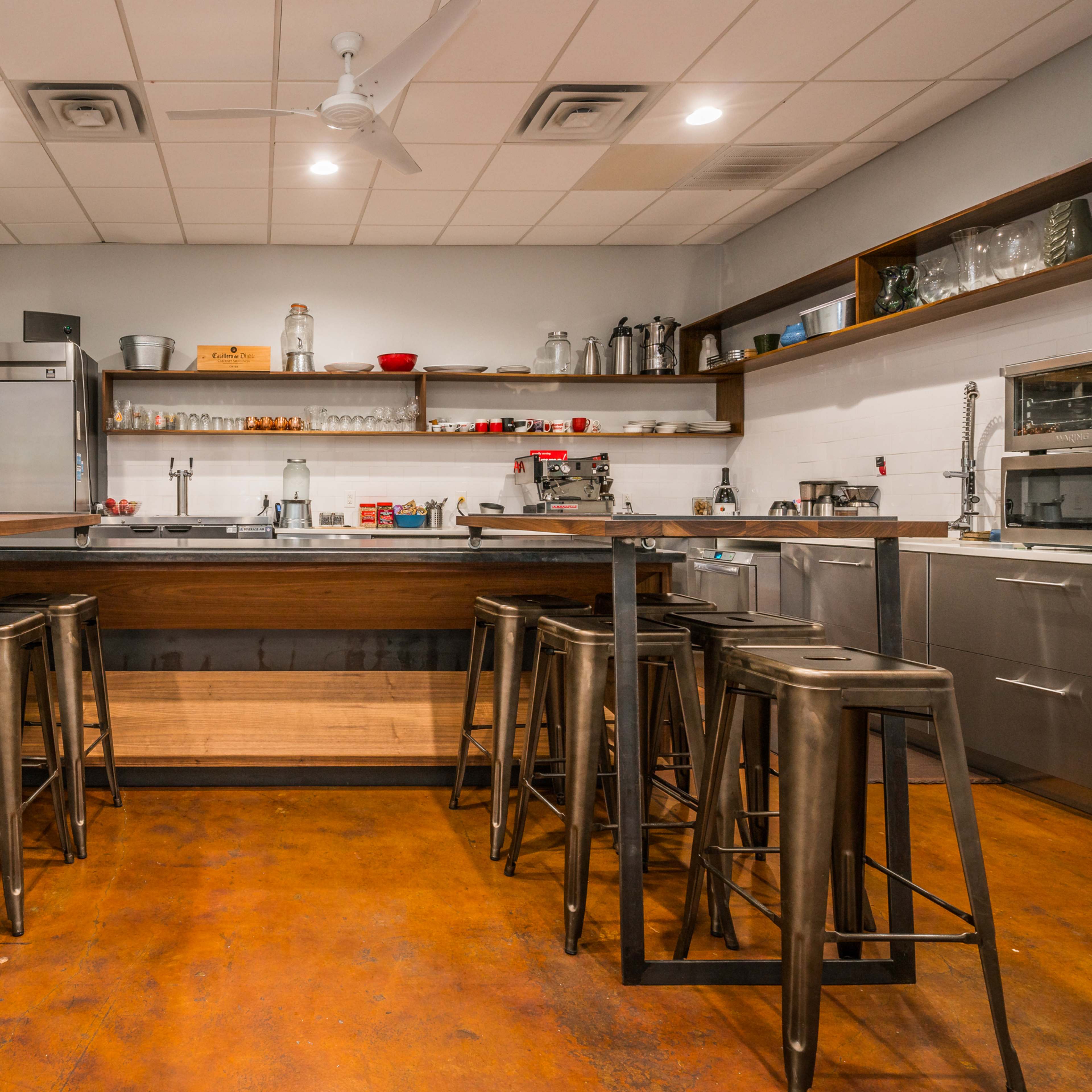 A modern kitchen with metal bar stools arranged around a wooden island and stainless steel appliances in a well-organized space.