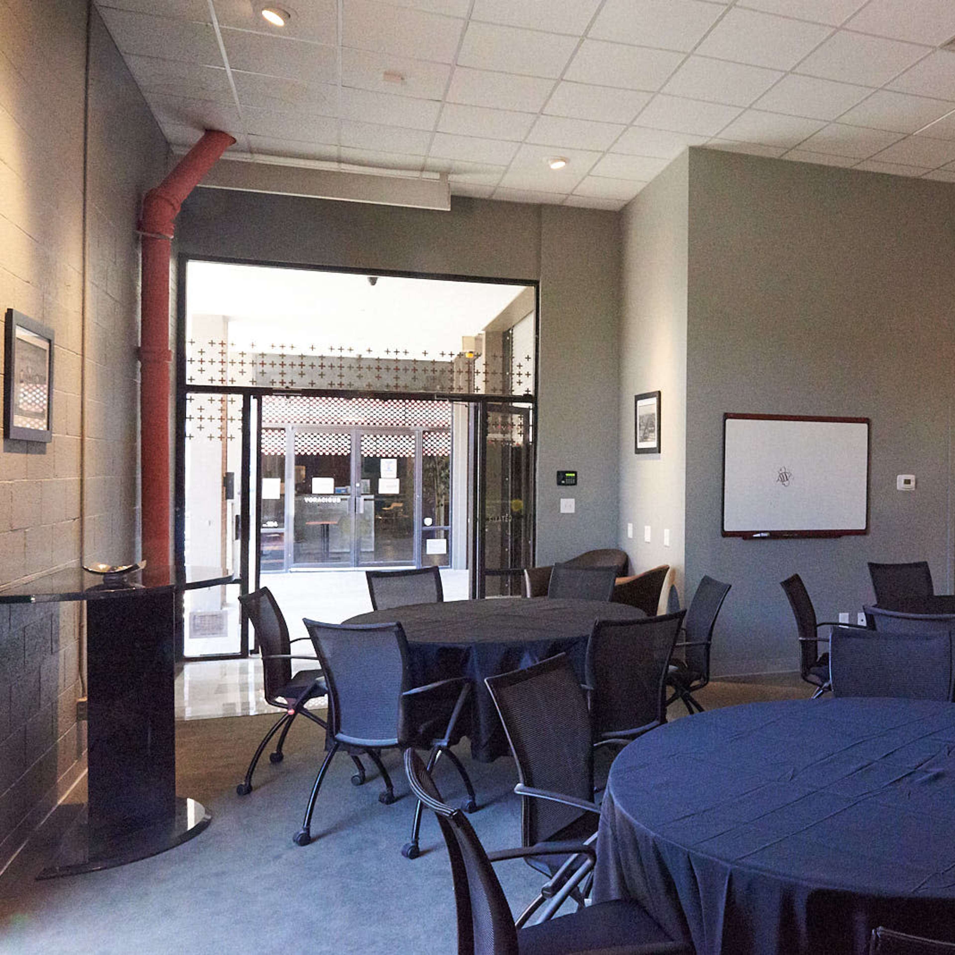 A meeting room with round tables covered in dark tablecloths and large windows revealing an outdoor area.