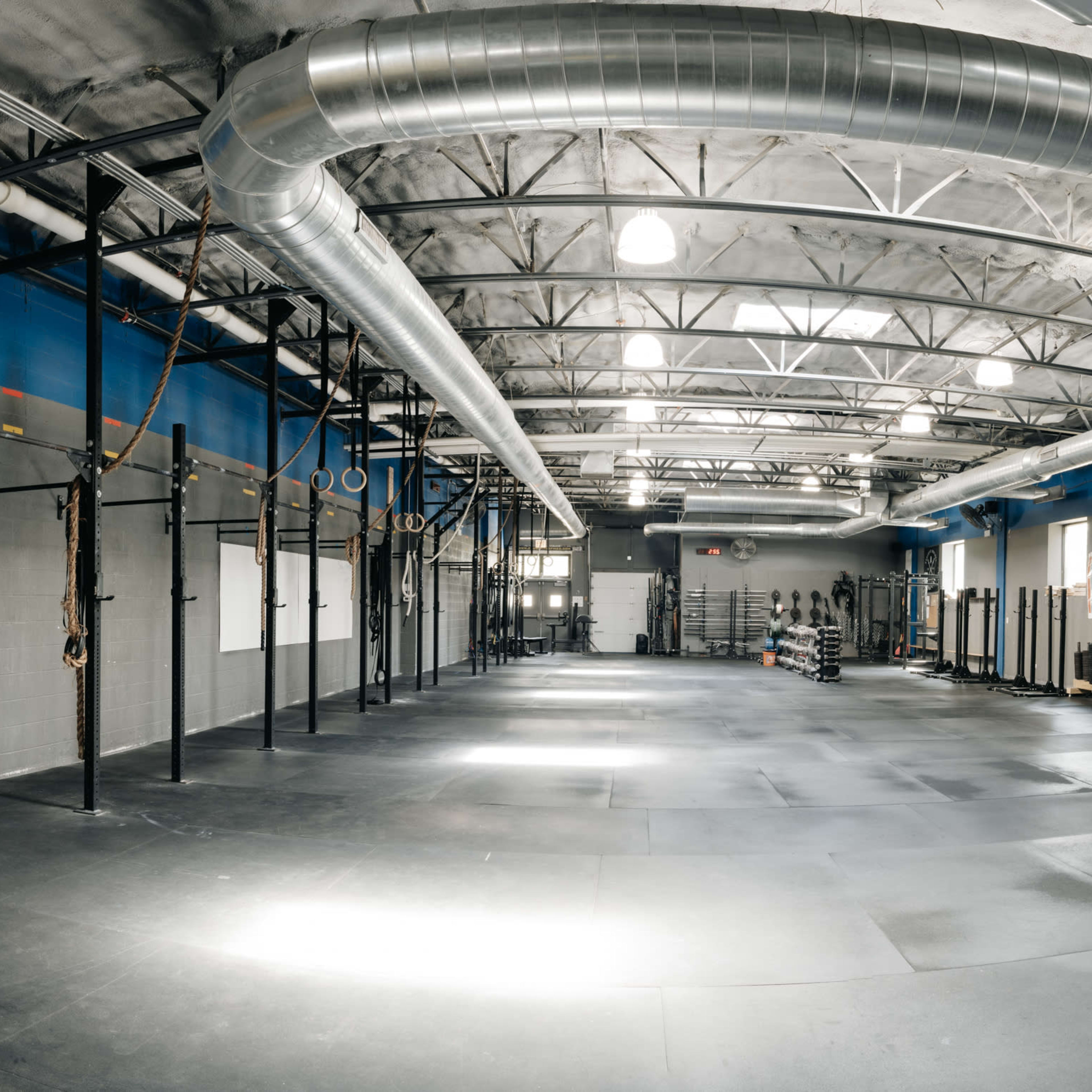 A spacious gym features black rubber flooring, wall-mounted pull-up bars, and neatly stacked weight plates along one side.