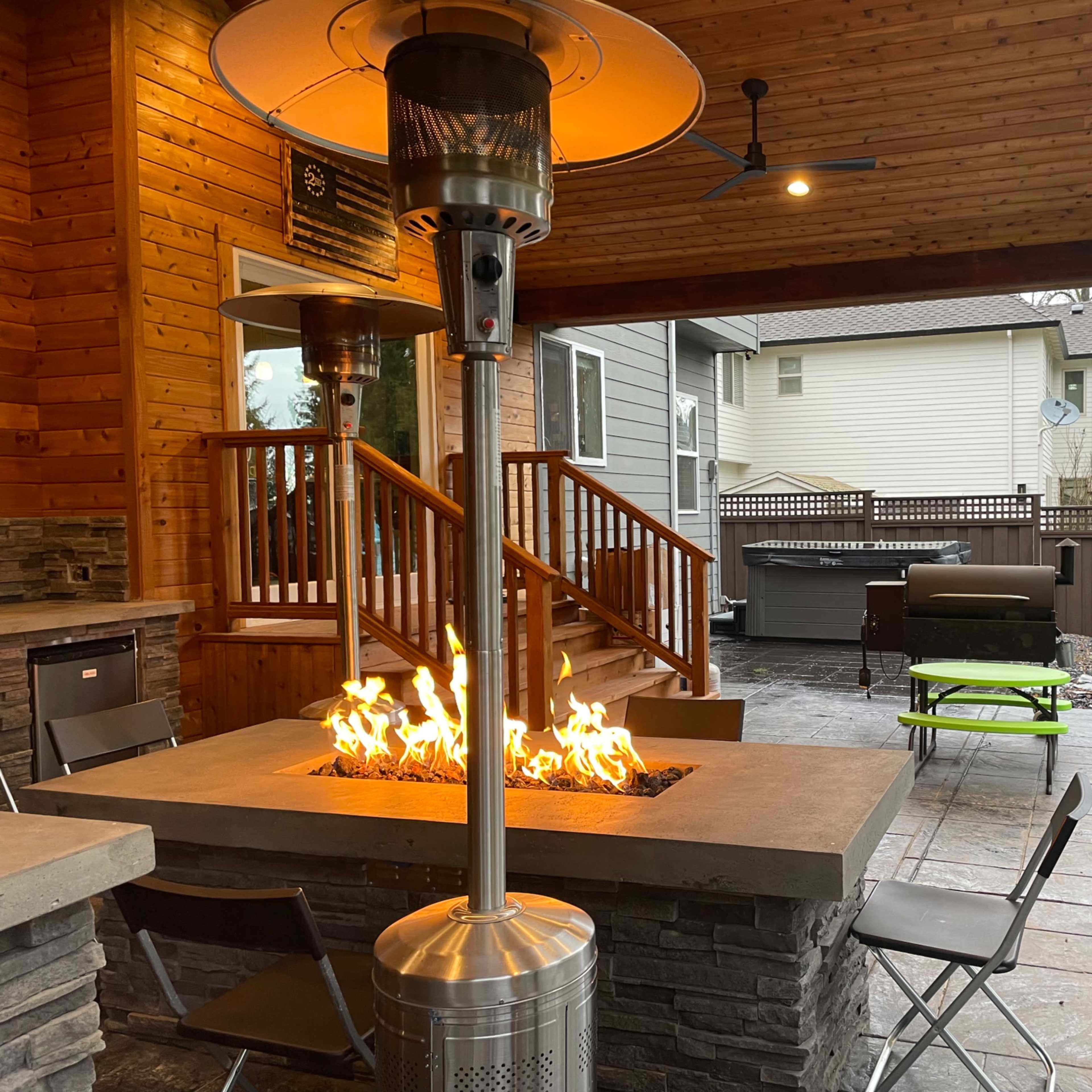 A covered patio area with a stone fire pit, outdoor seating, and a hot tub in the background.