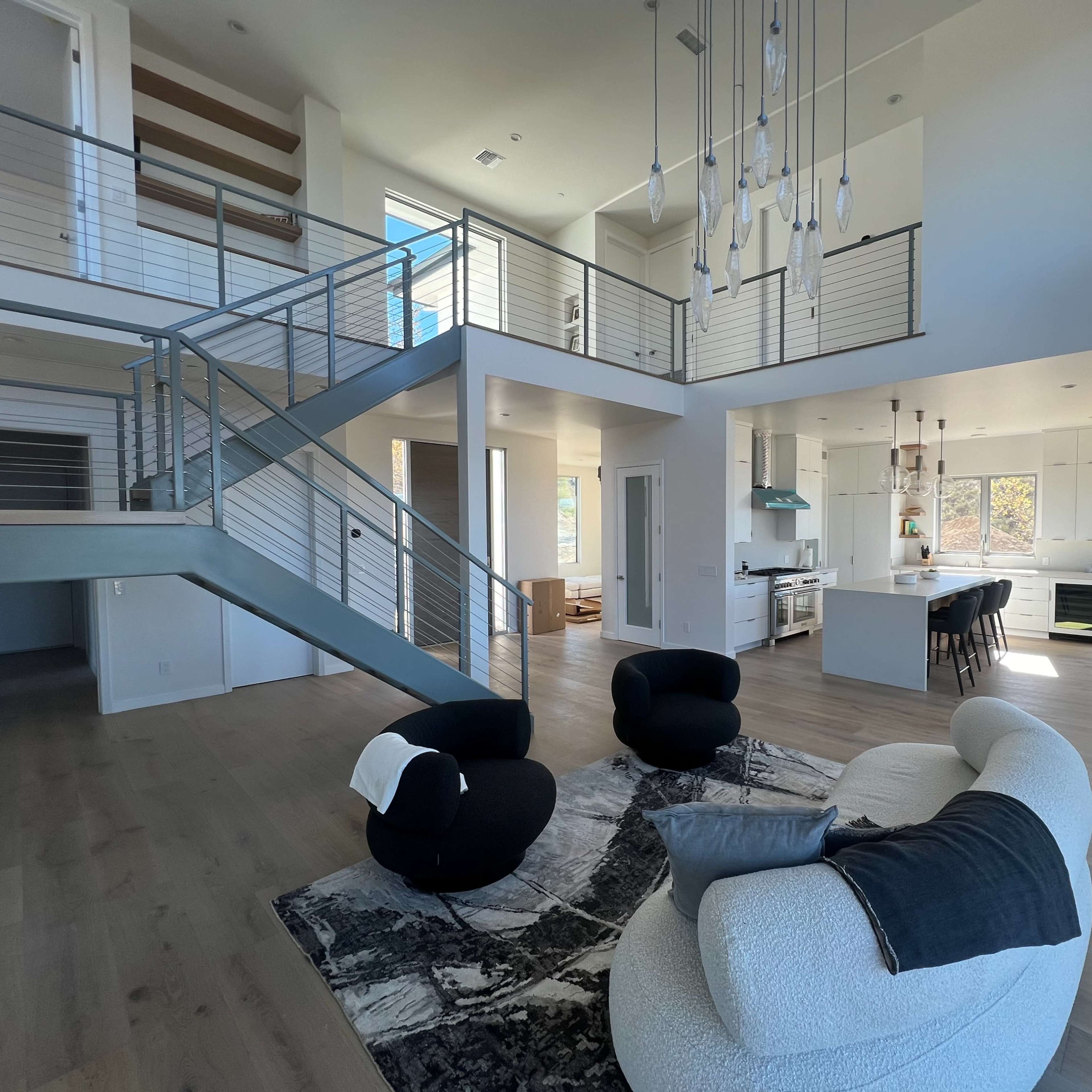 A modern, open-plan living space with a two-story ceiling, featuring a kitchen, dining area, and a staircase leading to the upper level.