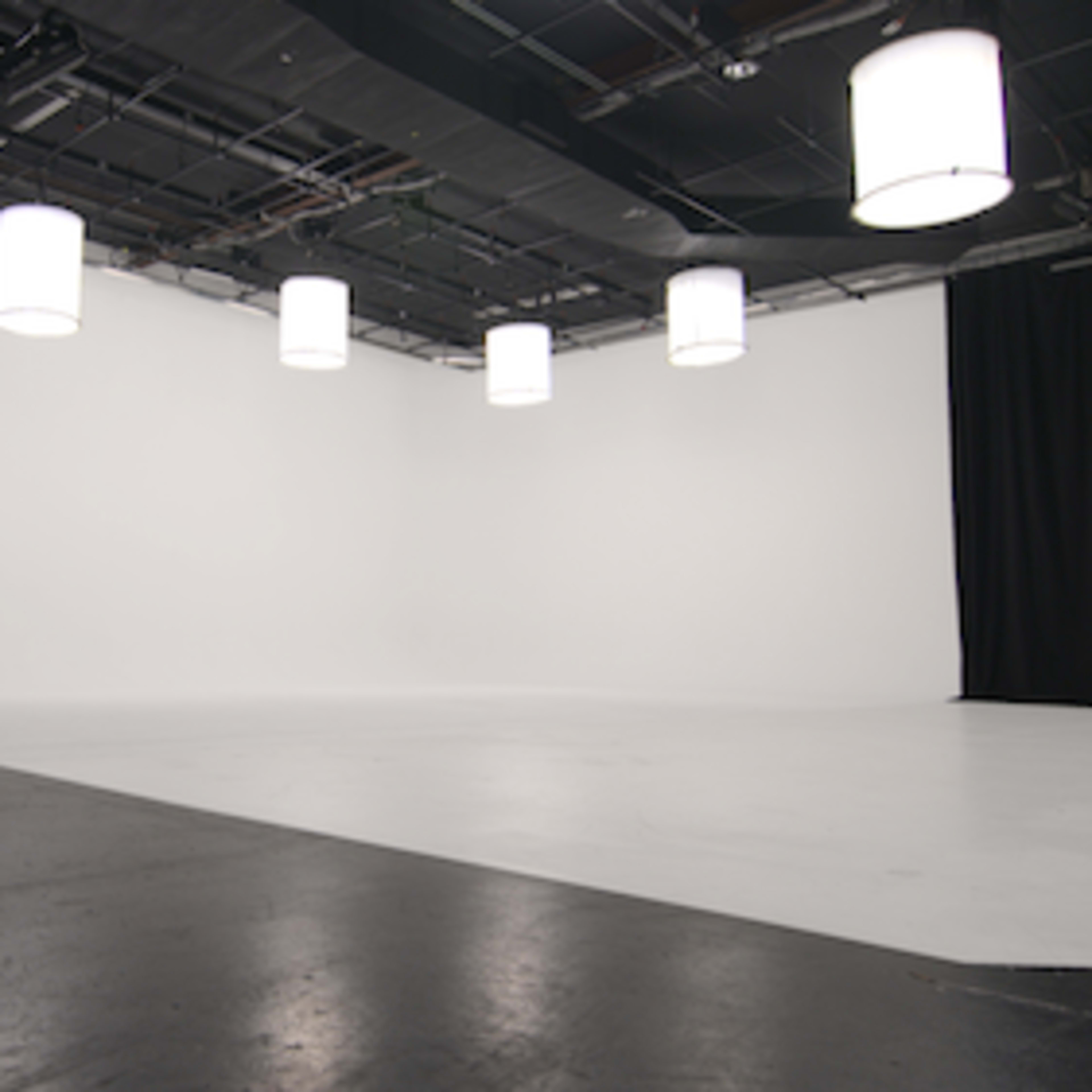 A large, empty studio space with a white backdrop and several hanging lights.