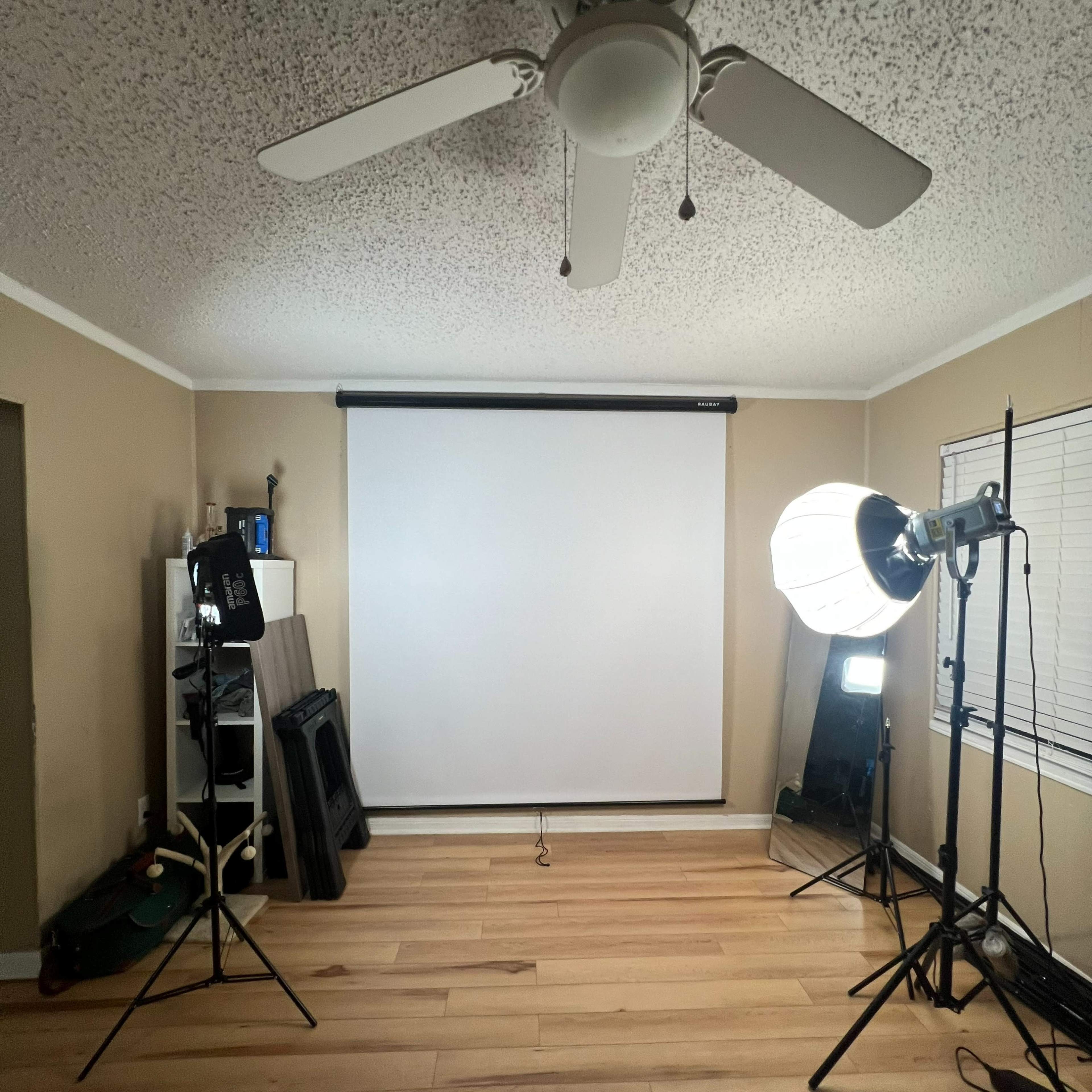 A well-lit room with a ceiling fan, a retractable projection screen, and two lighting setups on stands.