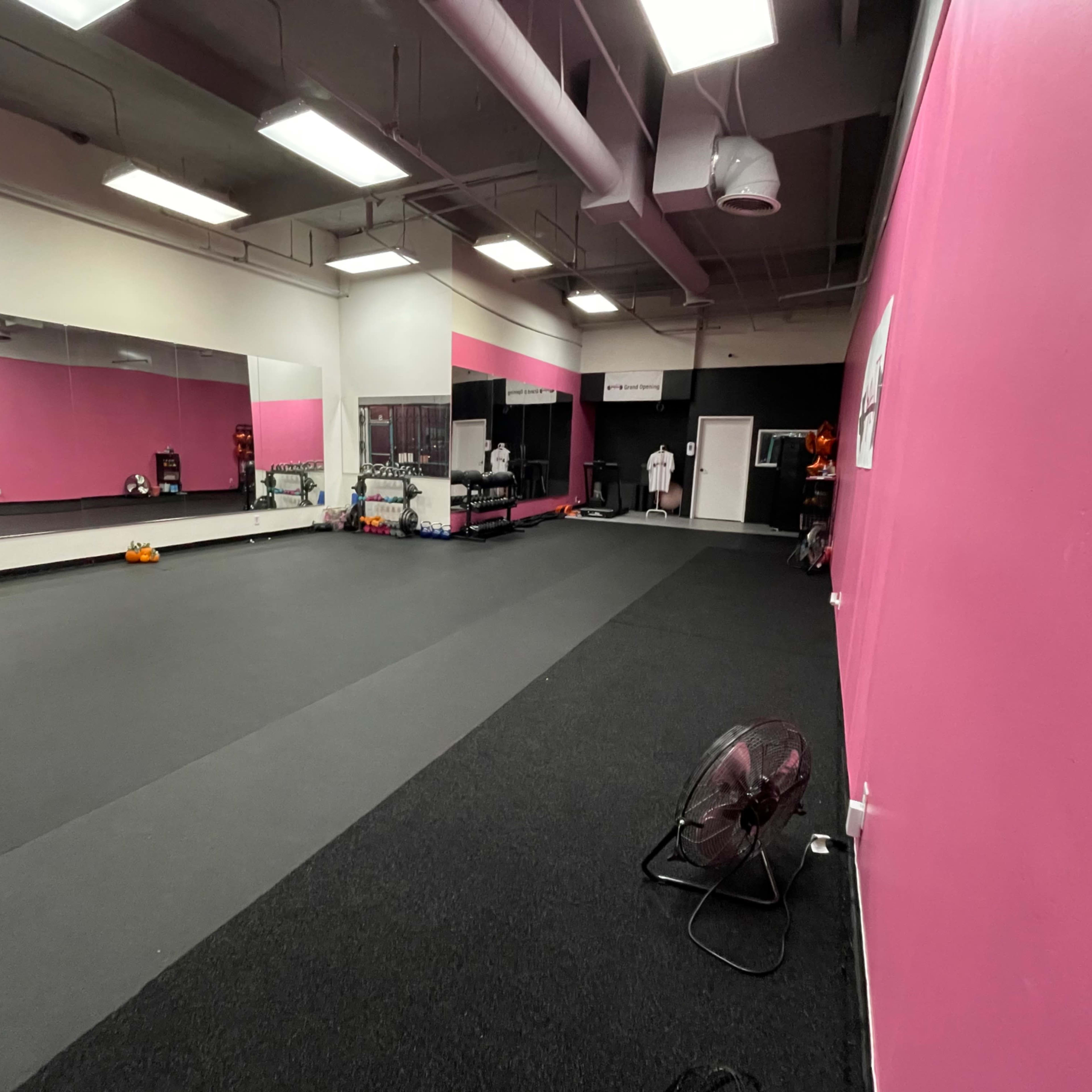 A spacious gym interior with pink walls, mirrors, and various workout equipment.
