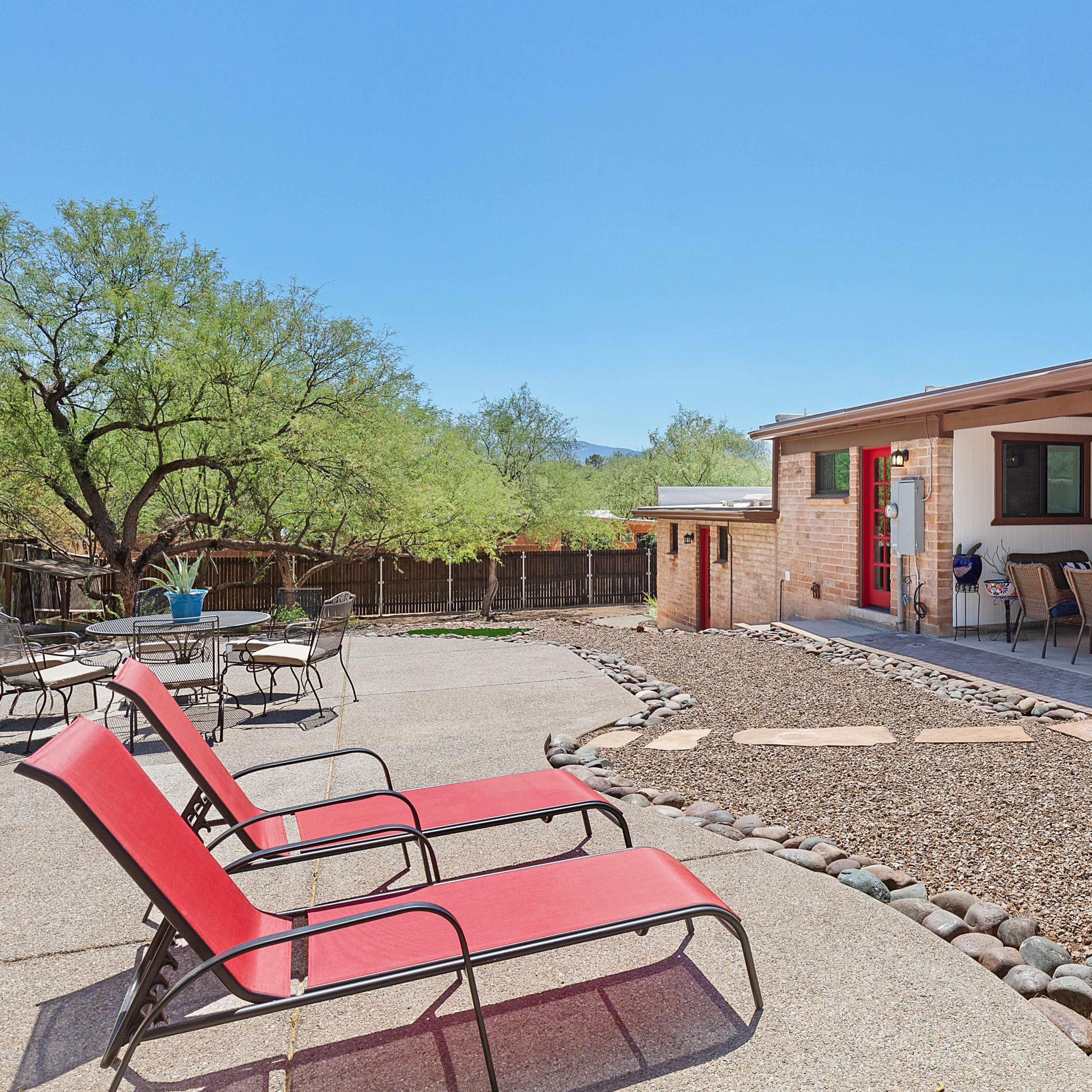 A patio area features red lounge chairs and a stone pathway leading to a home with red doors and a wide porch.