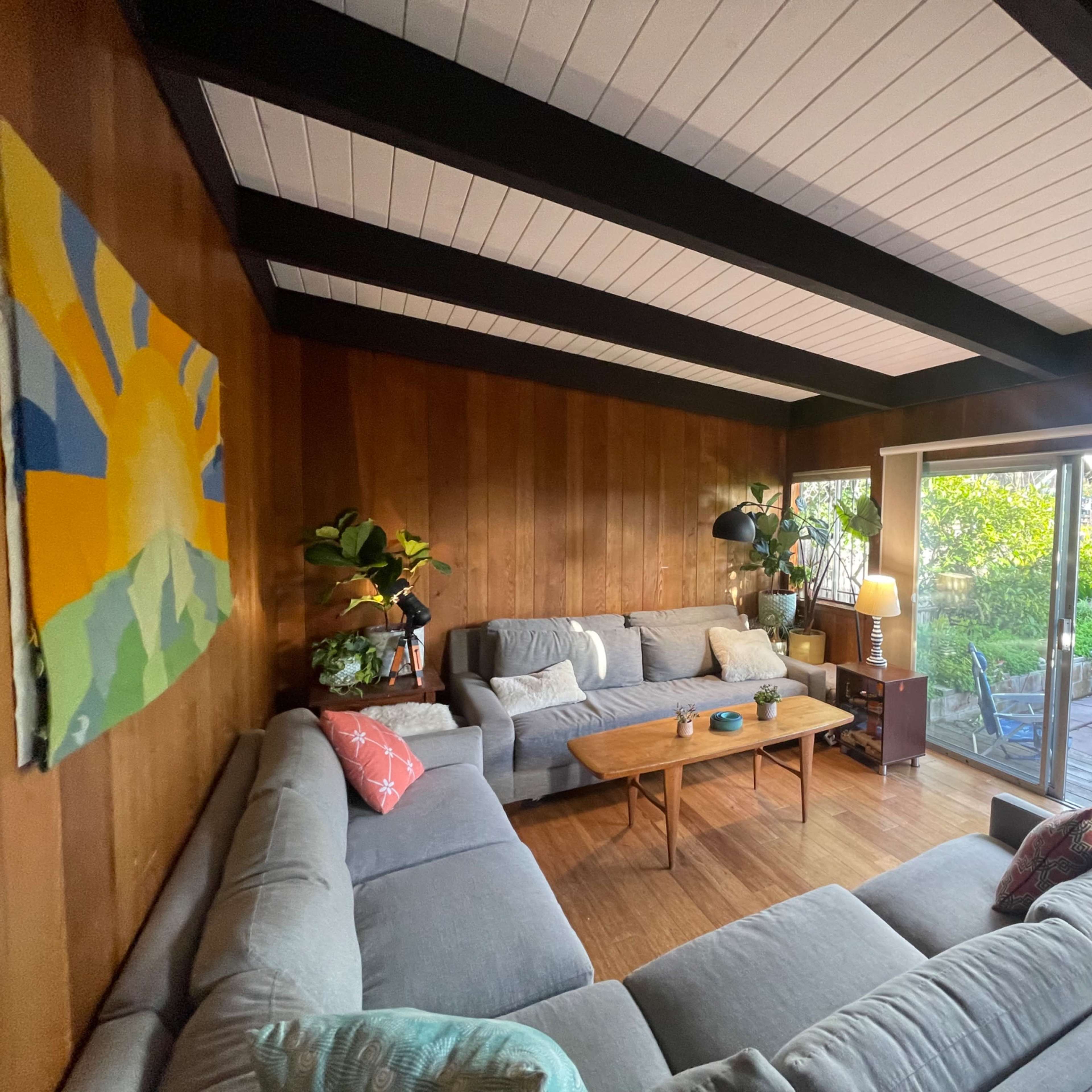 A modern living room features a sectional sofa arranged around a wooden coffee table, with large sliding glass doors opening to a backyard garden.