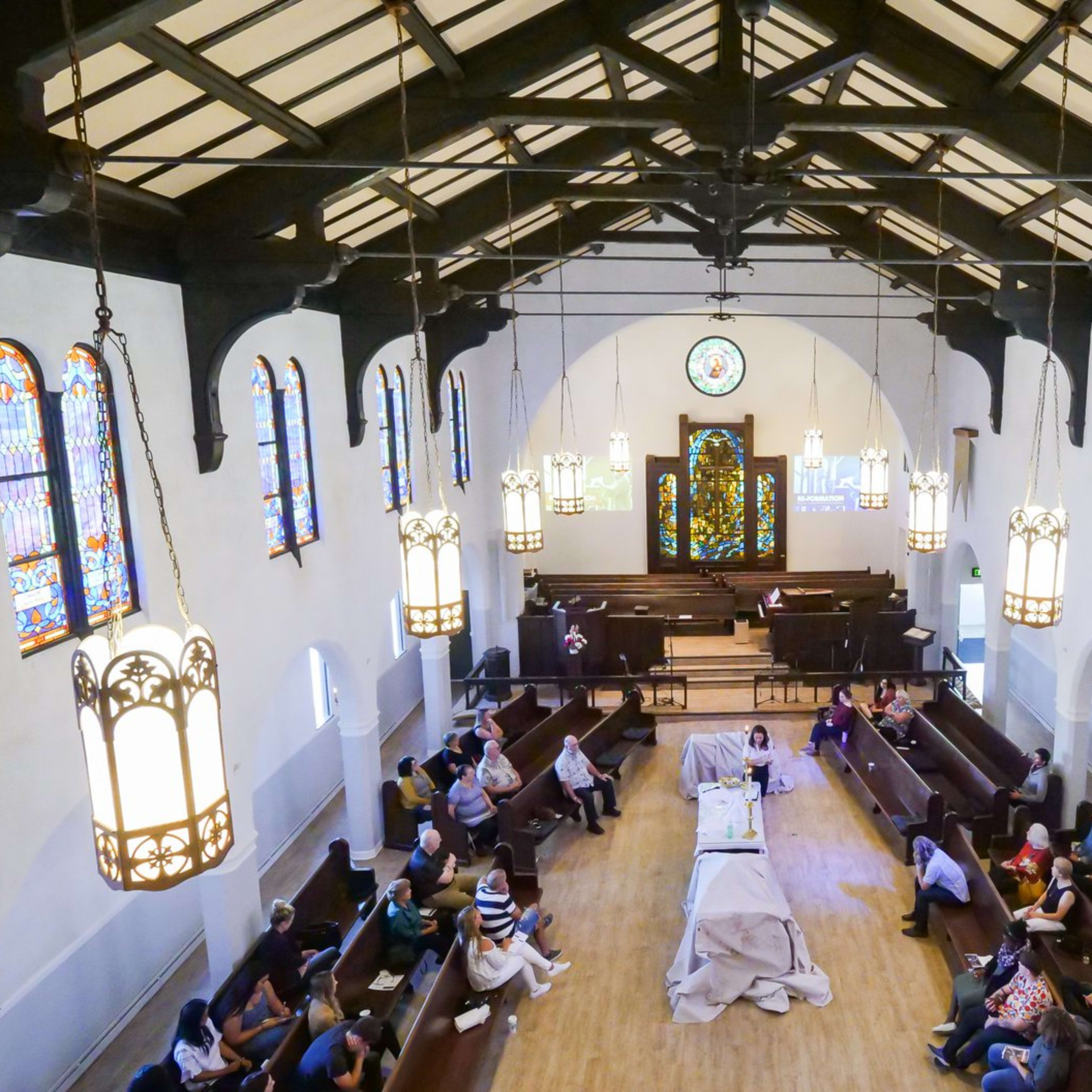 A spacious church interior with stained glass windows, featuring rows of seating and a central stage area where an event is taking place.