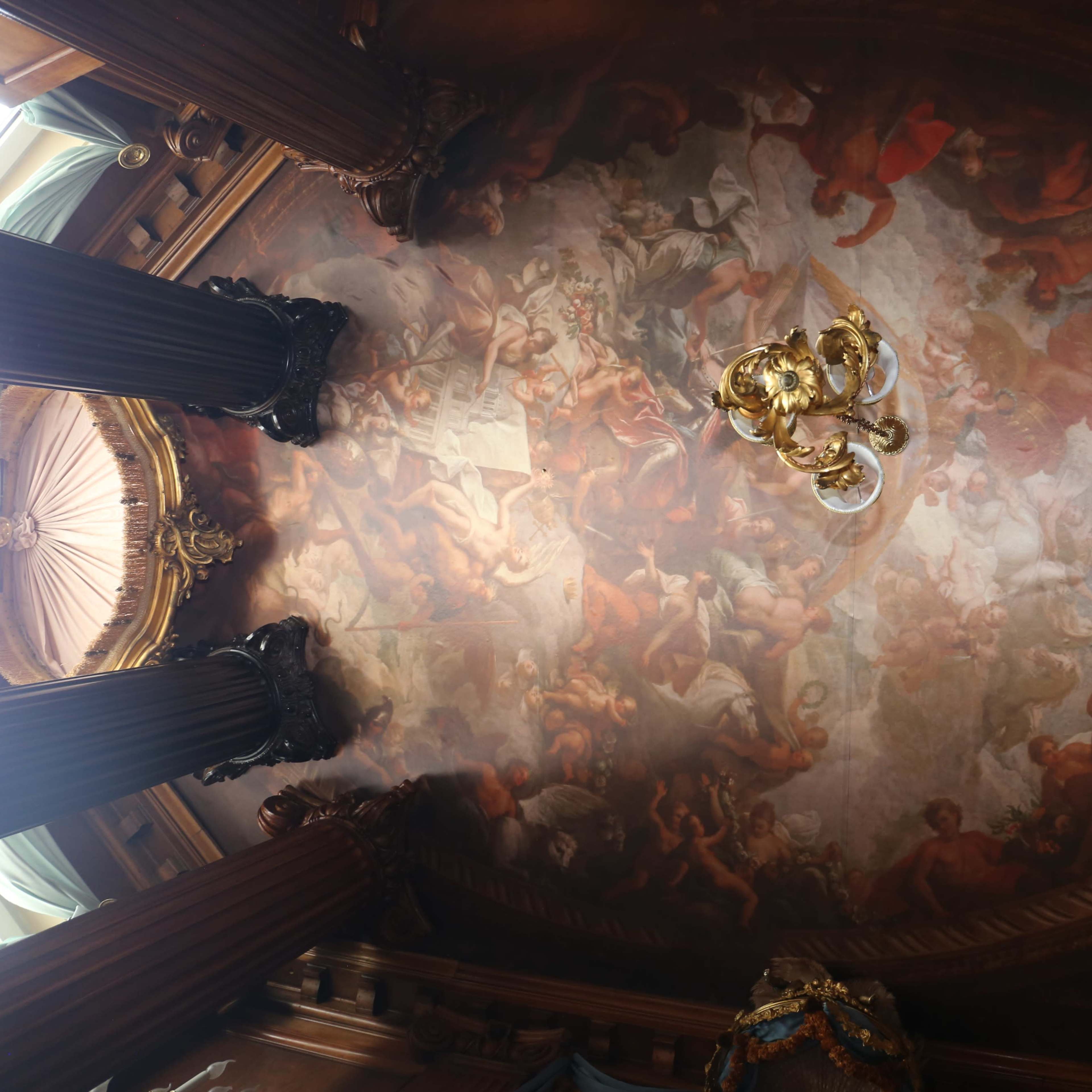 An ornate ceiling painted with classical figures and scenes, supported by decorative columns.
