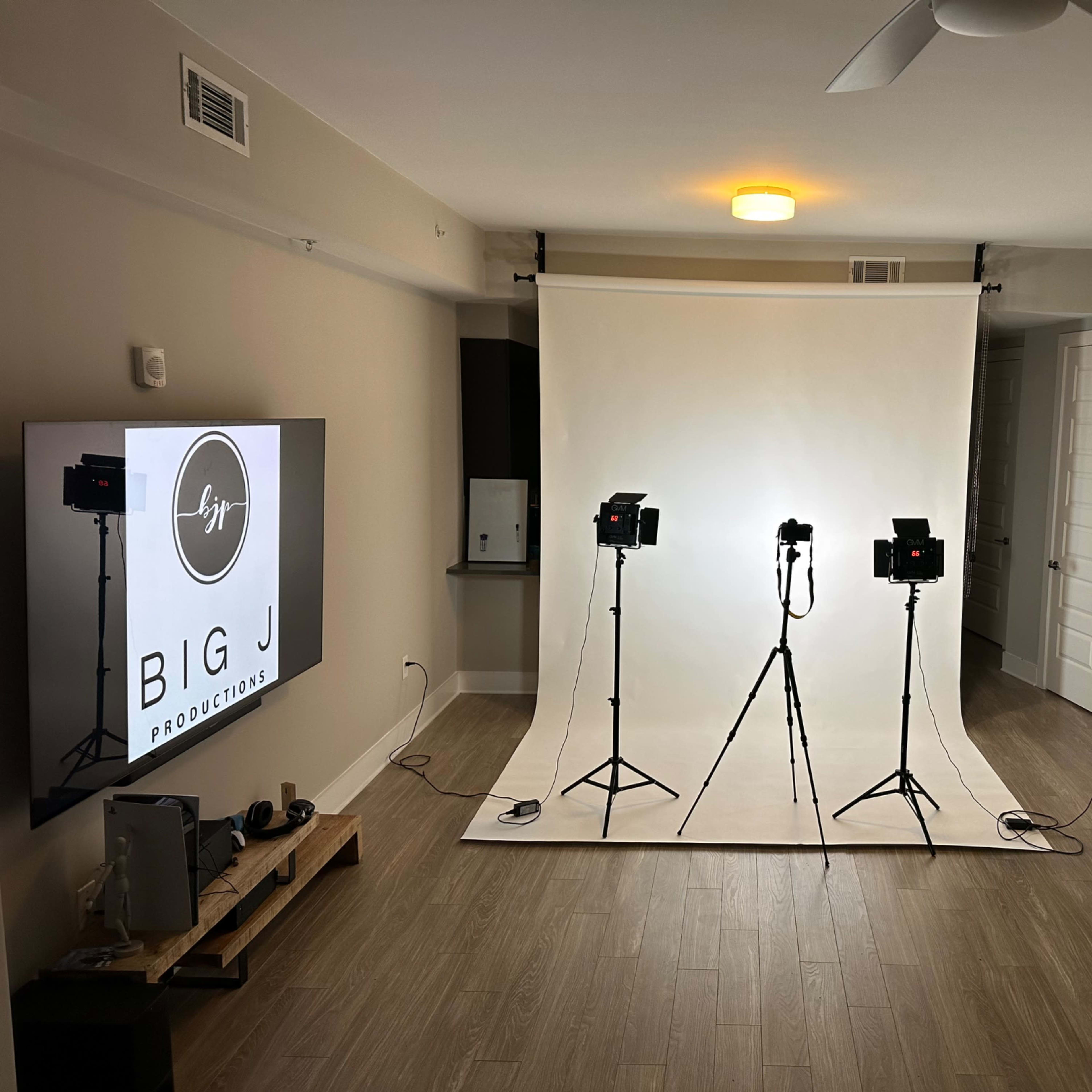 A studio setup with three tripods holding lights directed at a plain white backdrop in a minimalist room.