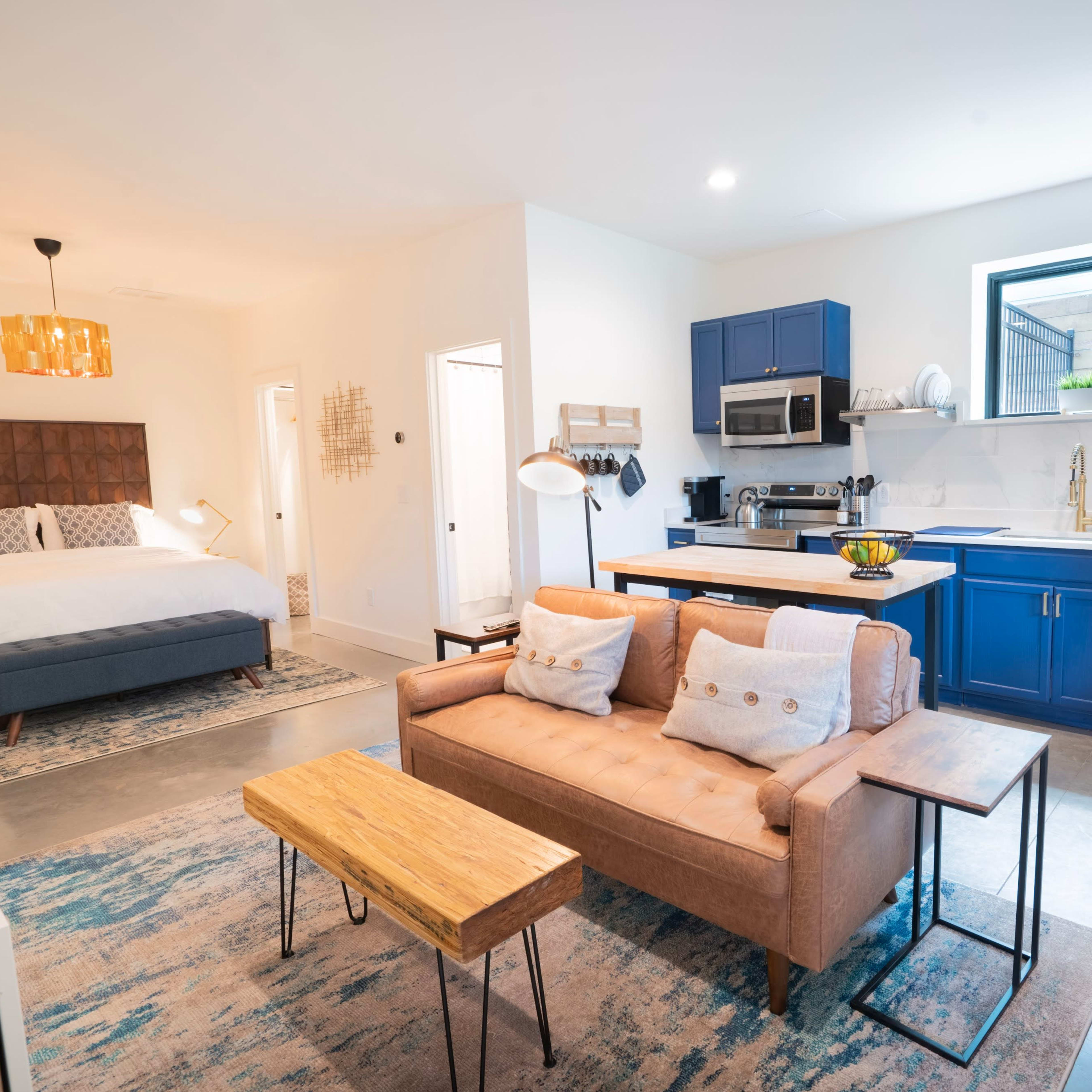 A modern, open-concept living space featuring a bedroom area with a bed, a kitchen with blue cabinetry, and a seating area with a sofa and coffee table.