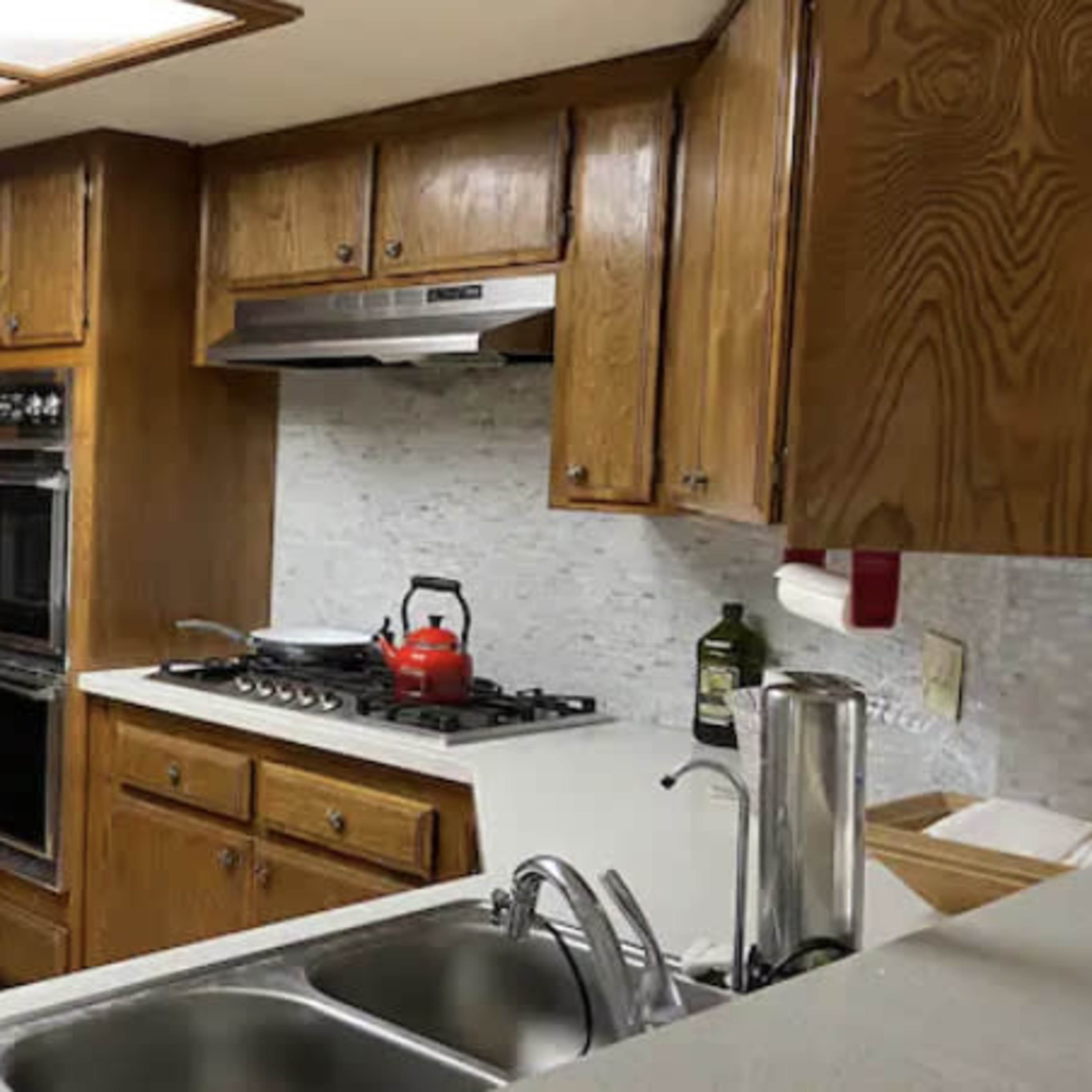 A kitchen with wooden cabinets, a double sink, an oven, a stovetop, and a microwave on the counter.
