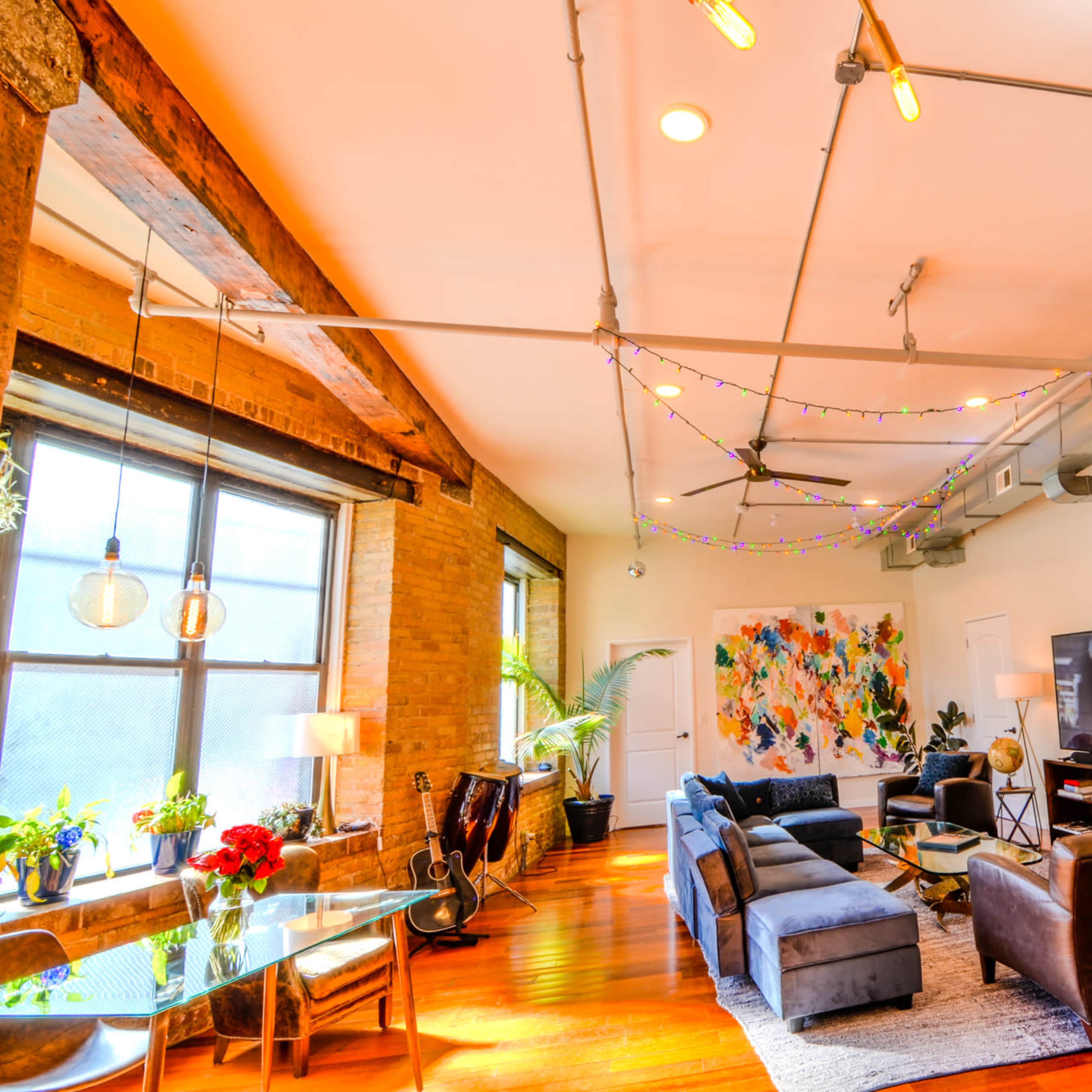 A spacious living room features exposed wooden beams, colorful artwork, a large television, and furniture arranged around a central rug.