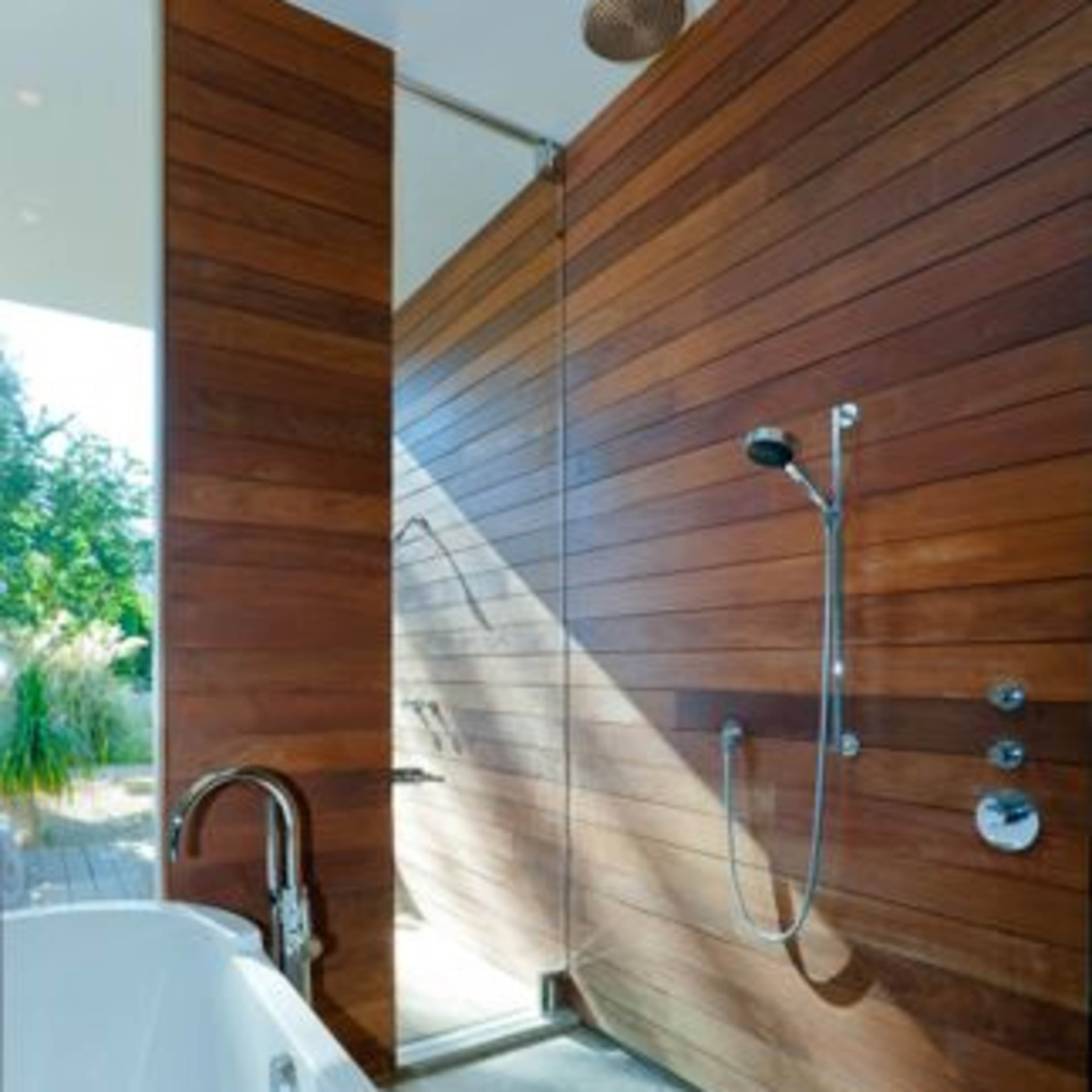 A modern bathroom with a wooden wall, a shower fixture on one side, and a freestanding bathtub partially covered with a towel.