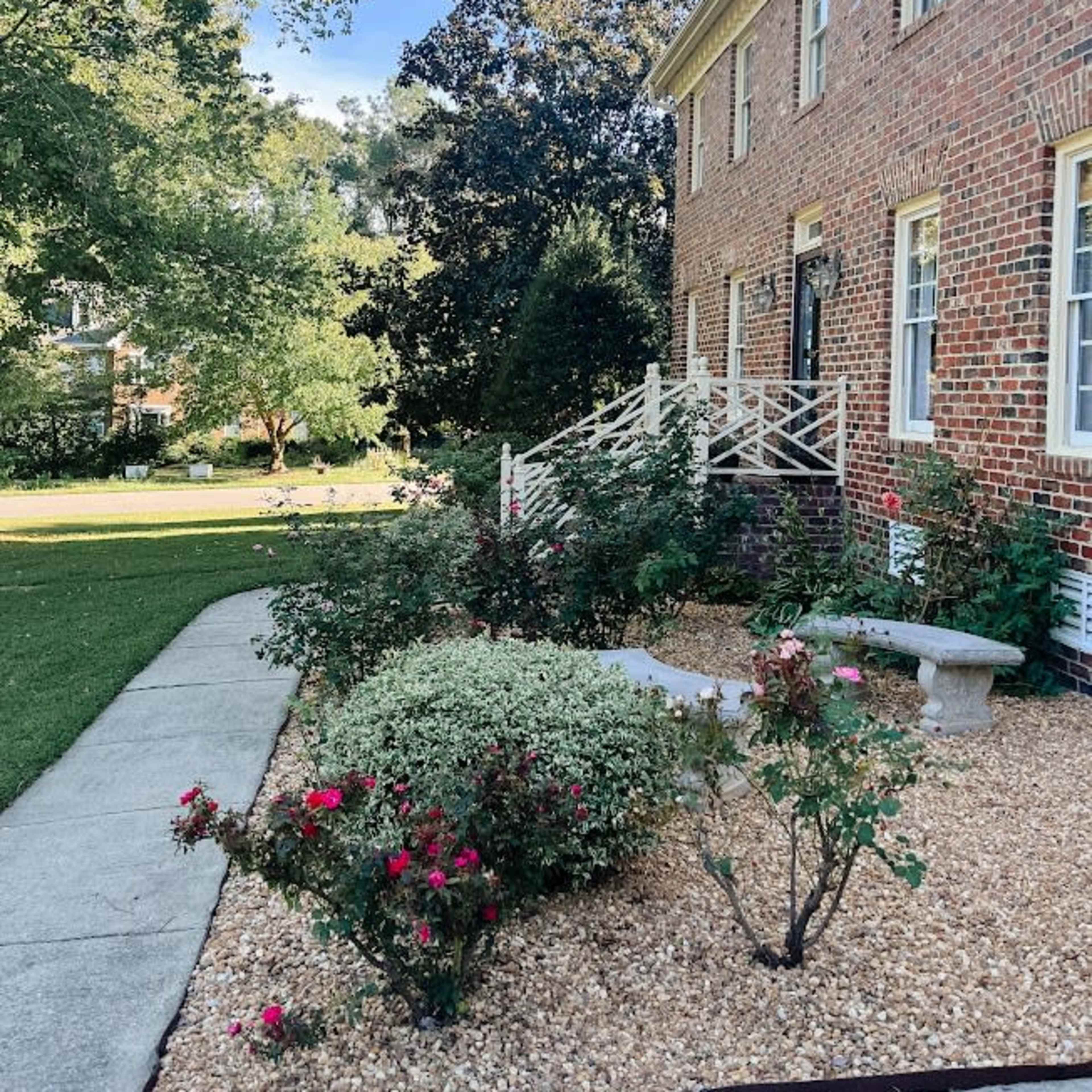 A brick house features a landscaped garden with flowers and gravel pathways leading to a set of steps.