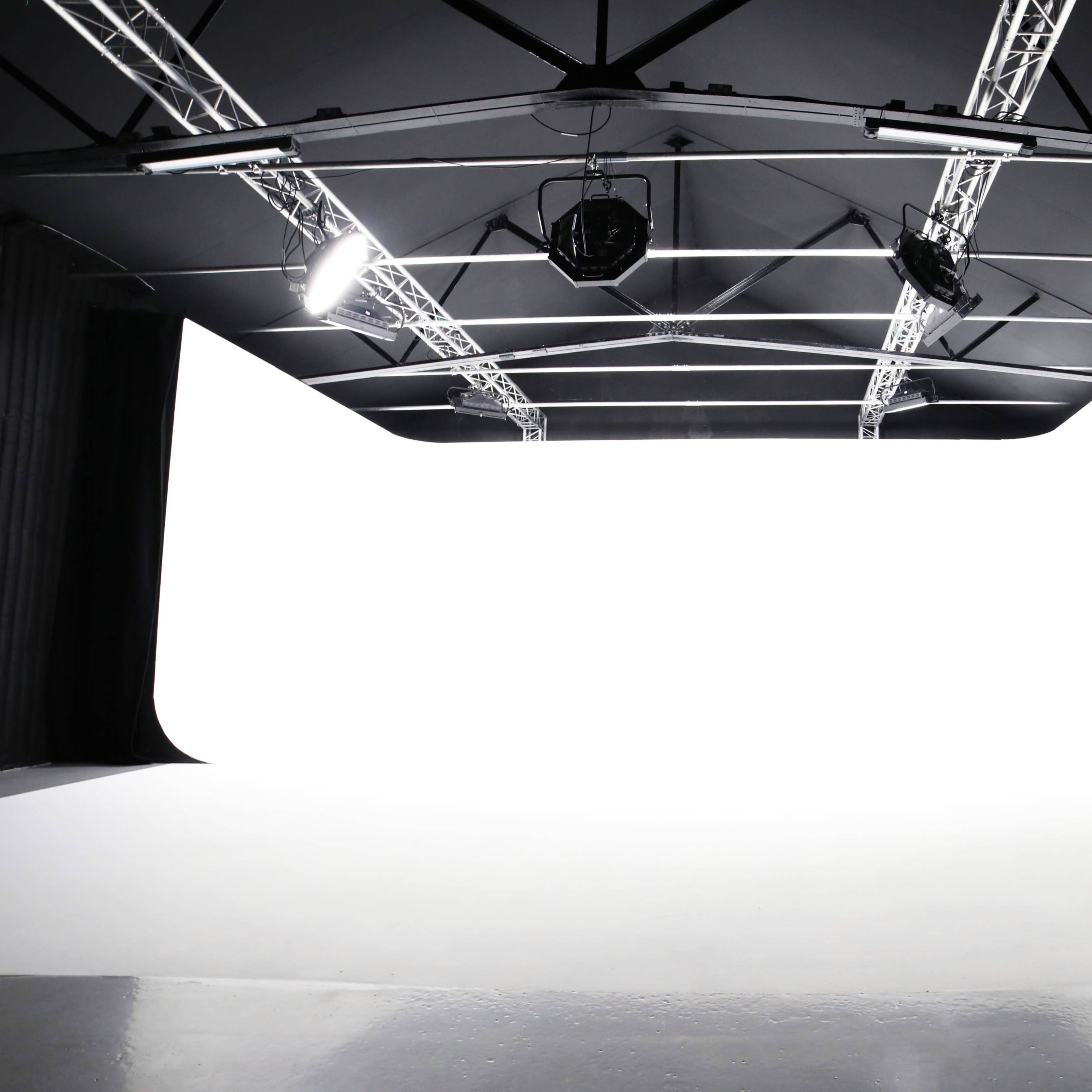 A spacious studio with a white backdrop, suspended lights, and a smooth floor.