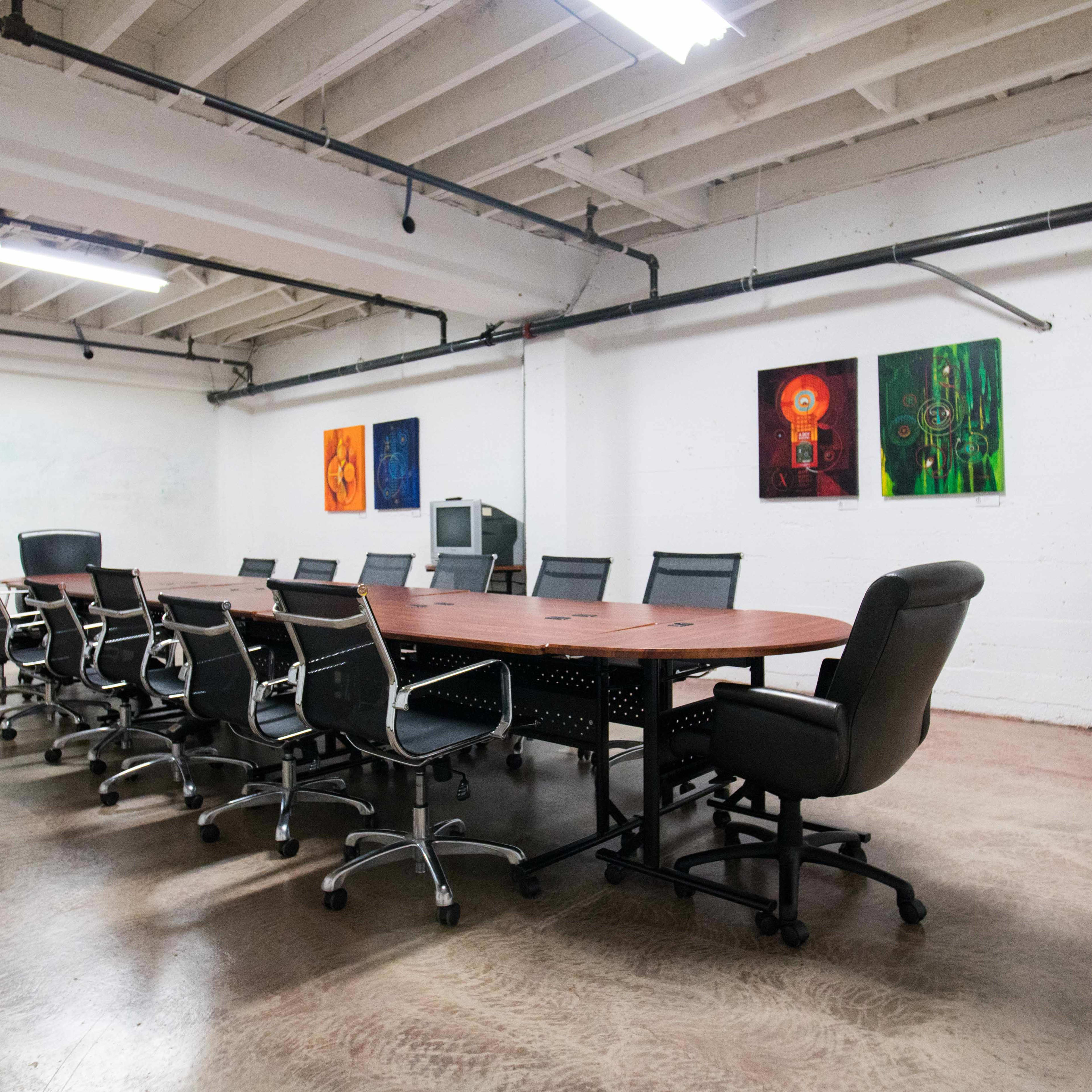 A large conference room features a long wooden table surrounded by office chairs, with colorful artwork on the walls.