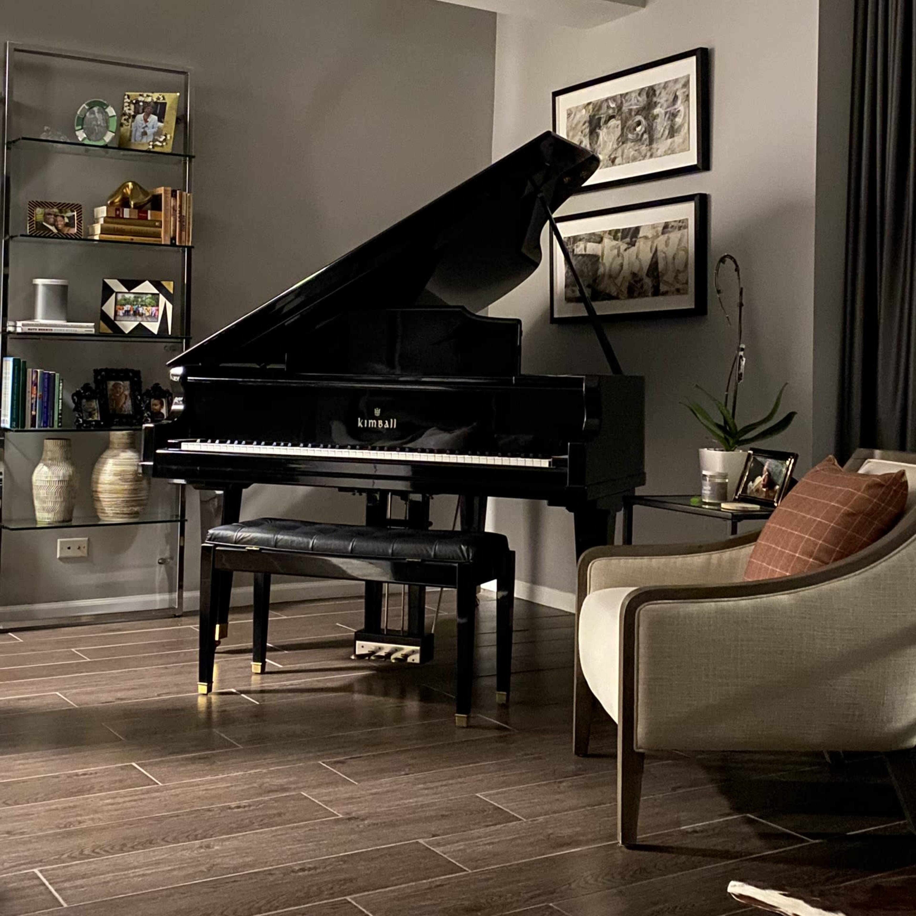 A black grand piano with its lid raised sits next to a modern armchair and a small table in a softly lit living room.