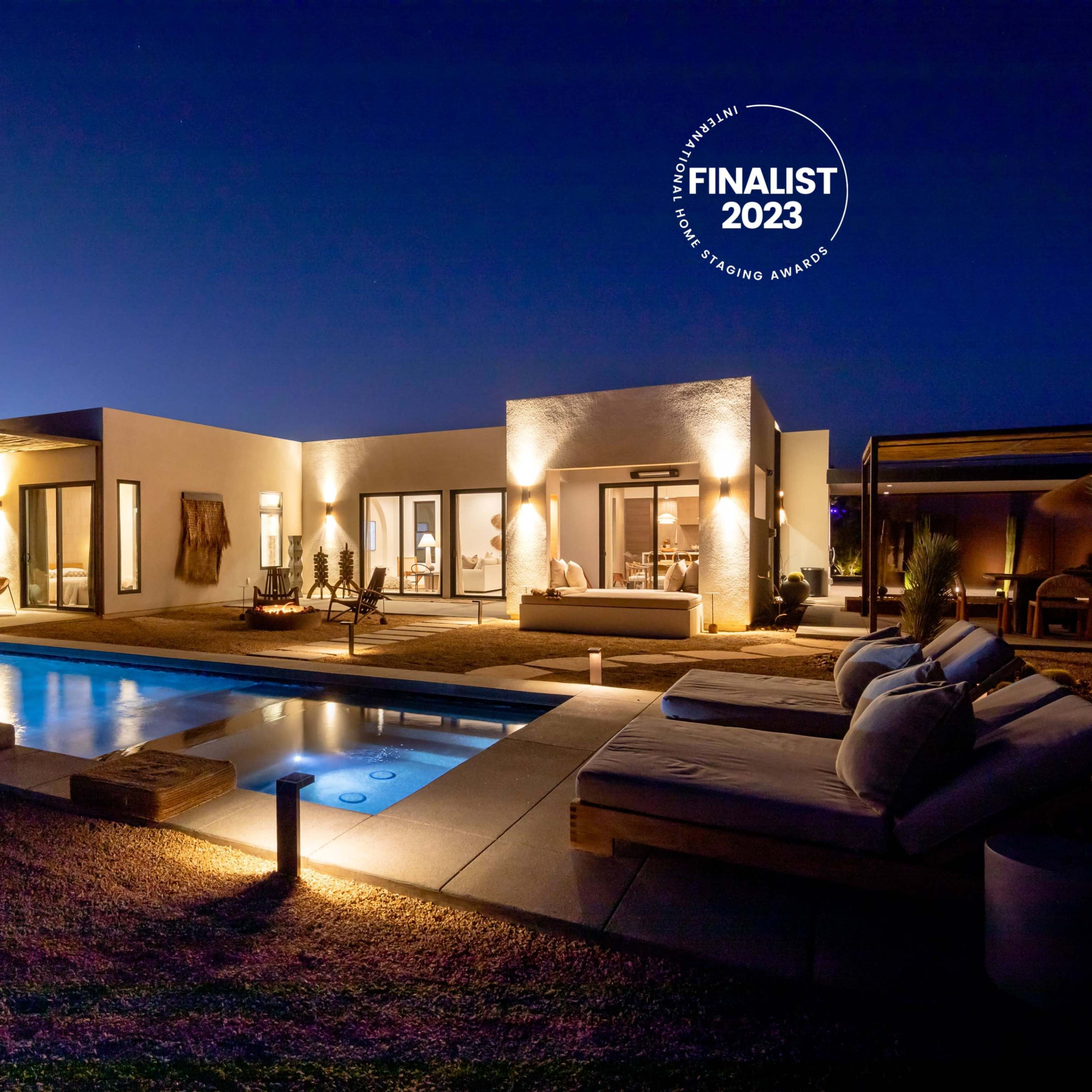 A modern villa with a pool and outdoor seating is illuminated at night, showcasing its design and ambiance.