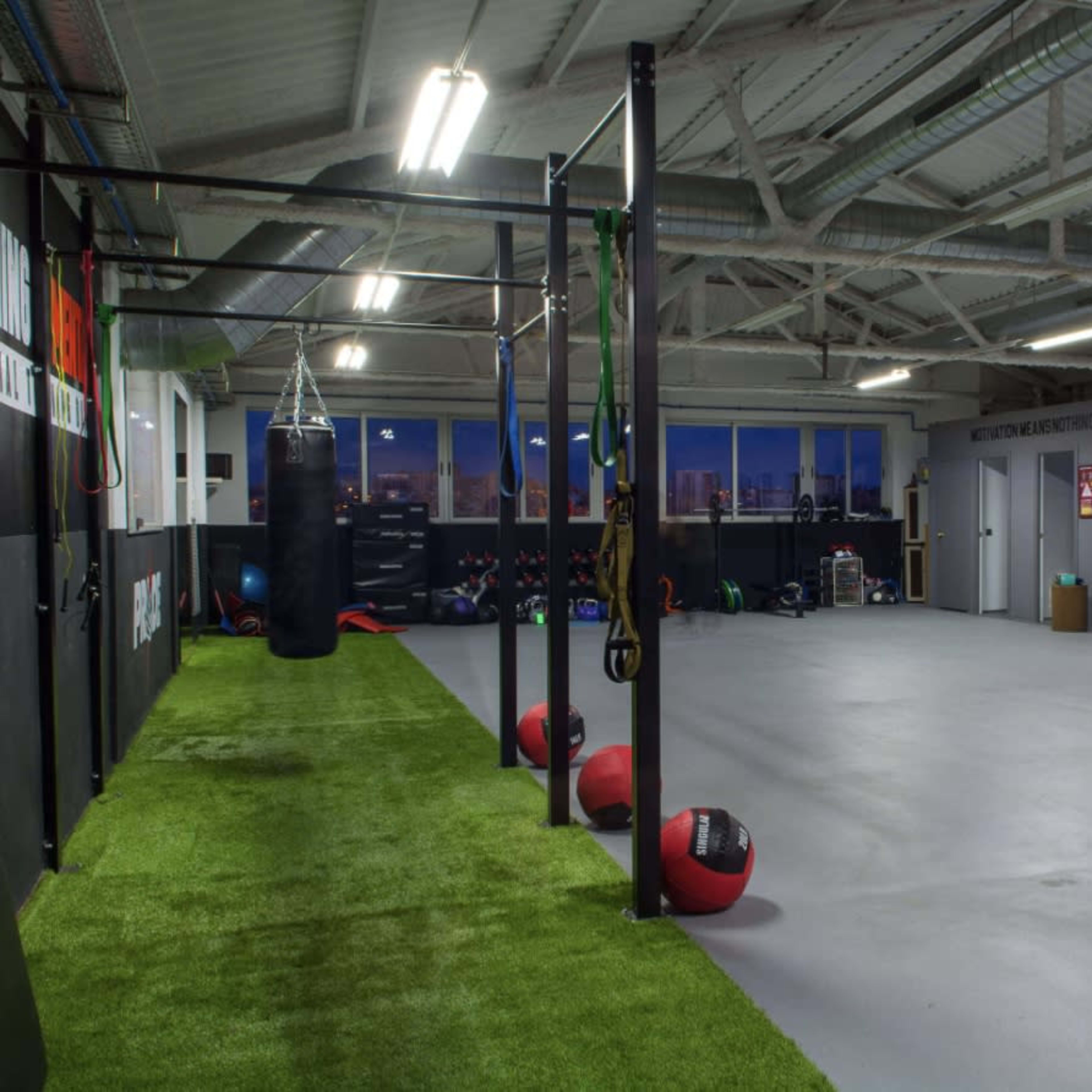 A spacious gym with exercise equipment, boxing bags, and a green turf area.