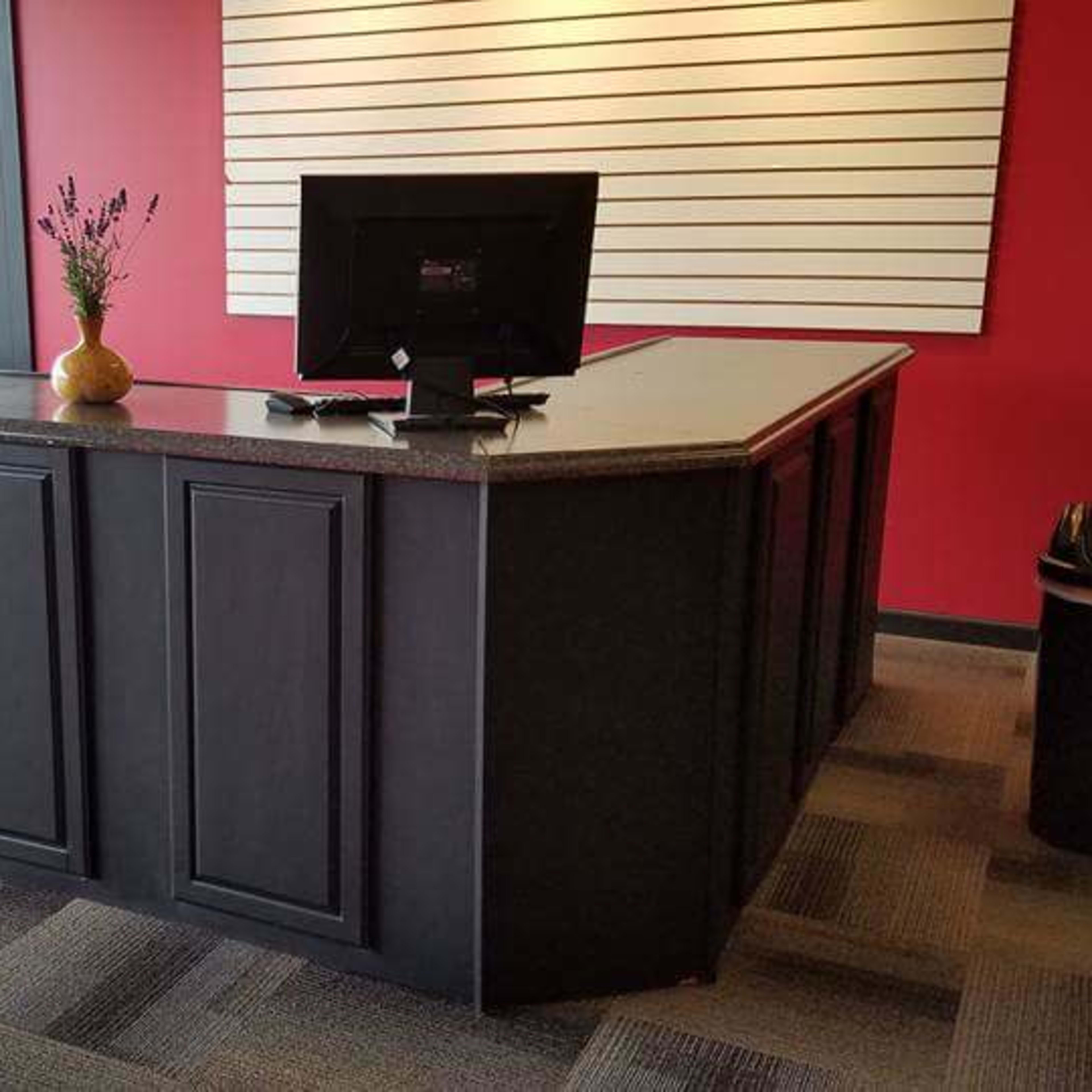 A black reception desk with a granite countertop, backed by a red wall and featuring a monitor on top.
