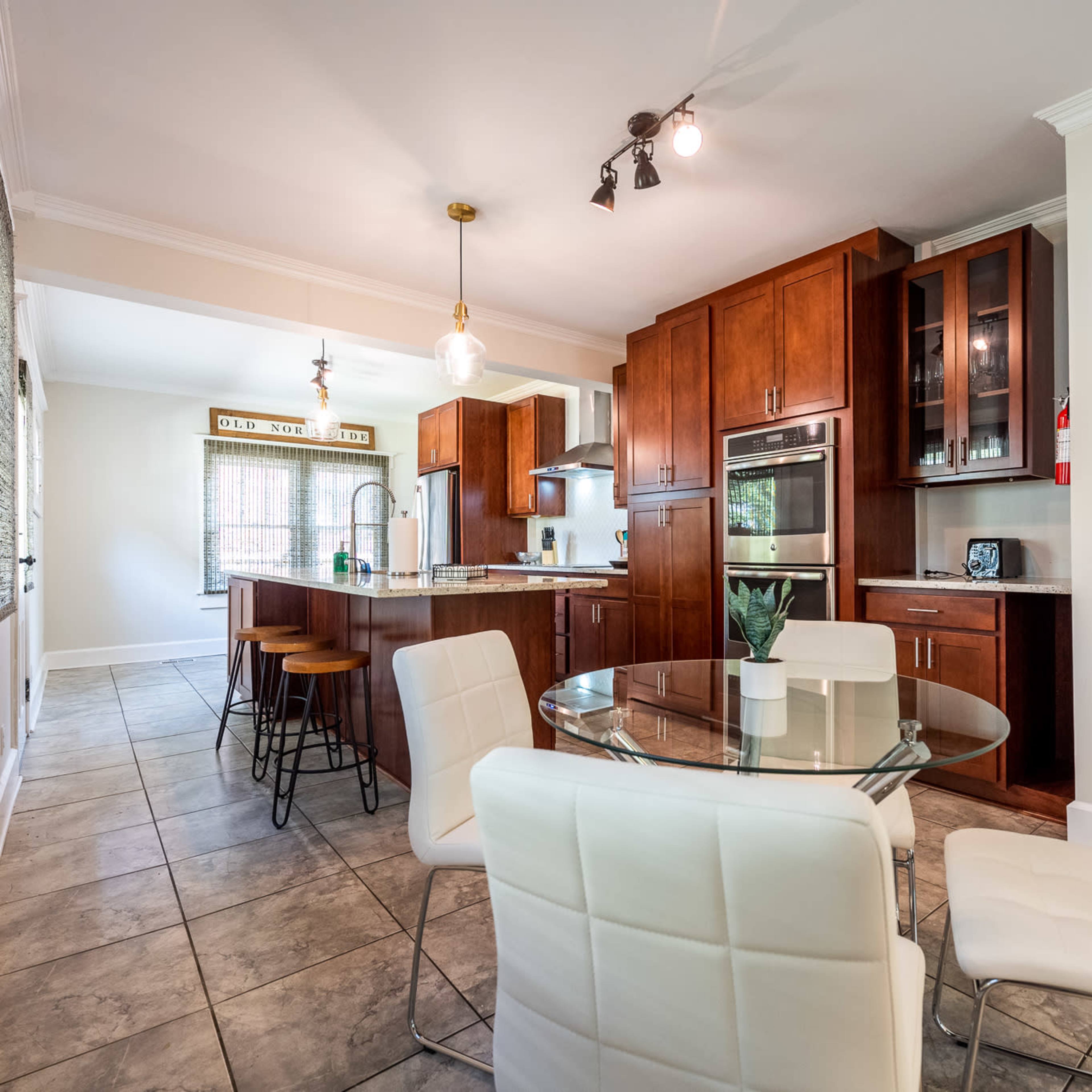 A modern kitchen and dining area with wooden cabinets, a glass dining table, and white chairs.