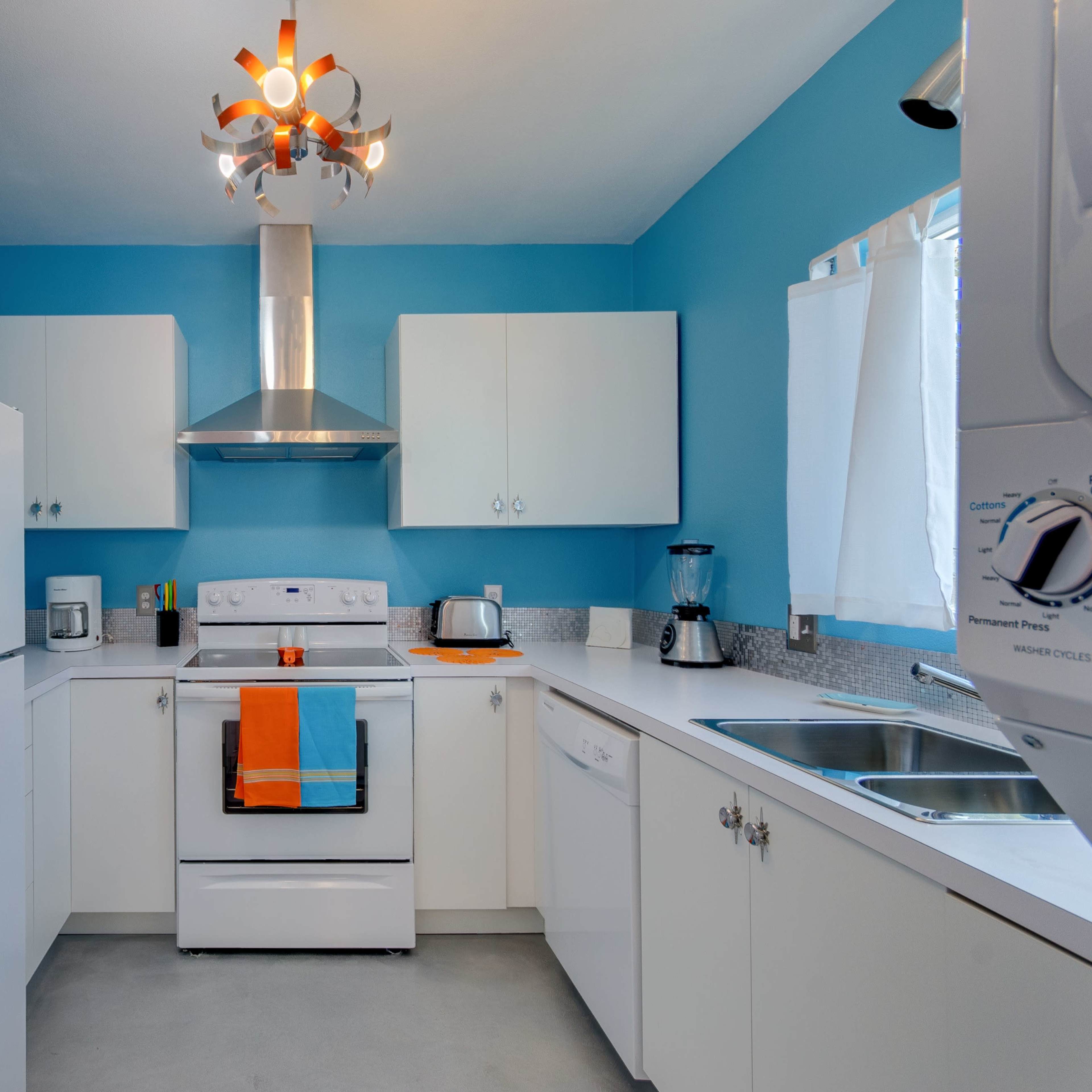A modern kitchen featuring white cabinets, a blue accent wall, and stainless steel appliances.