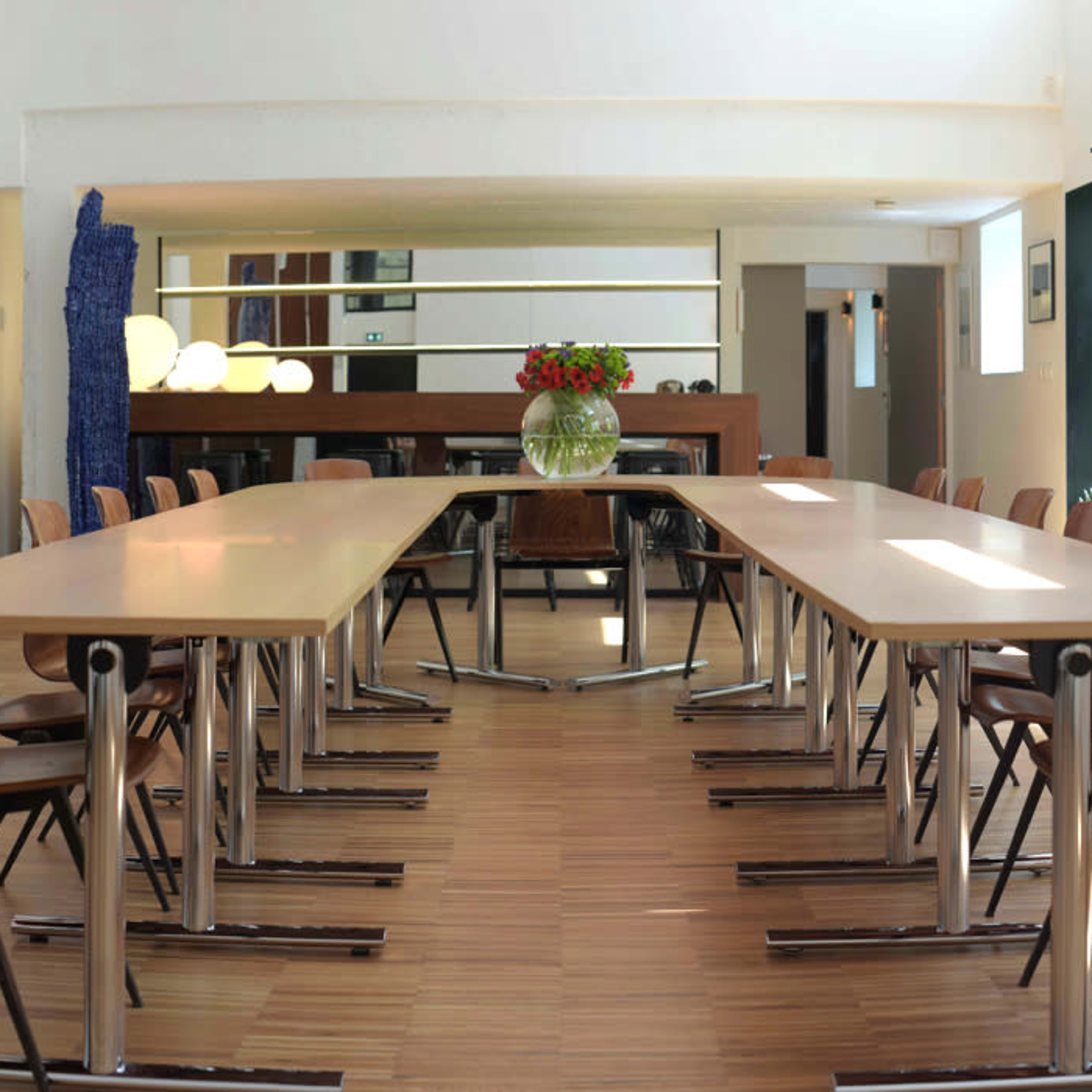 A spacious conference room features a long table set with chairs, illuminated by natural light from large windows.