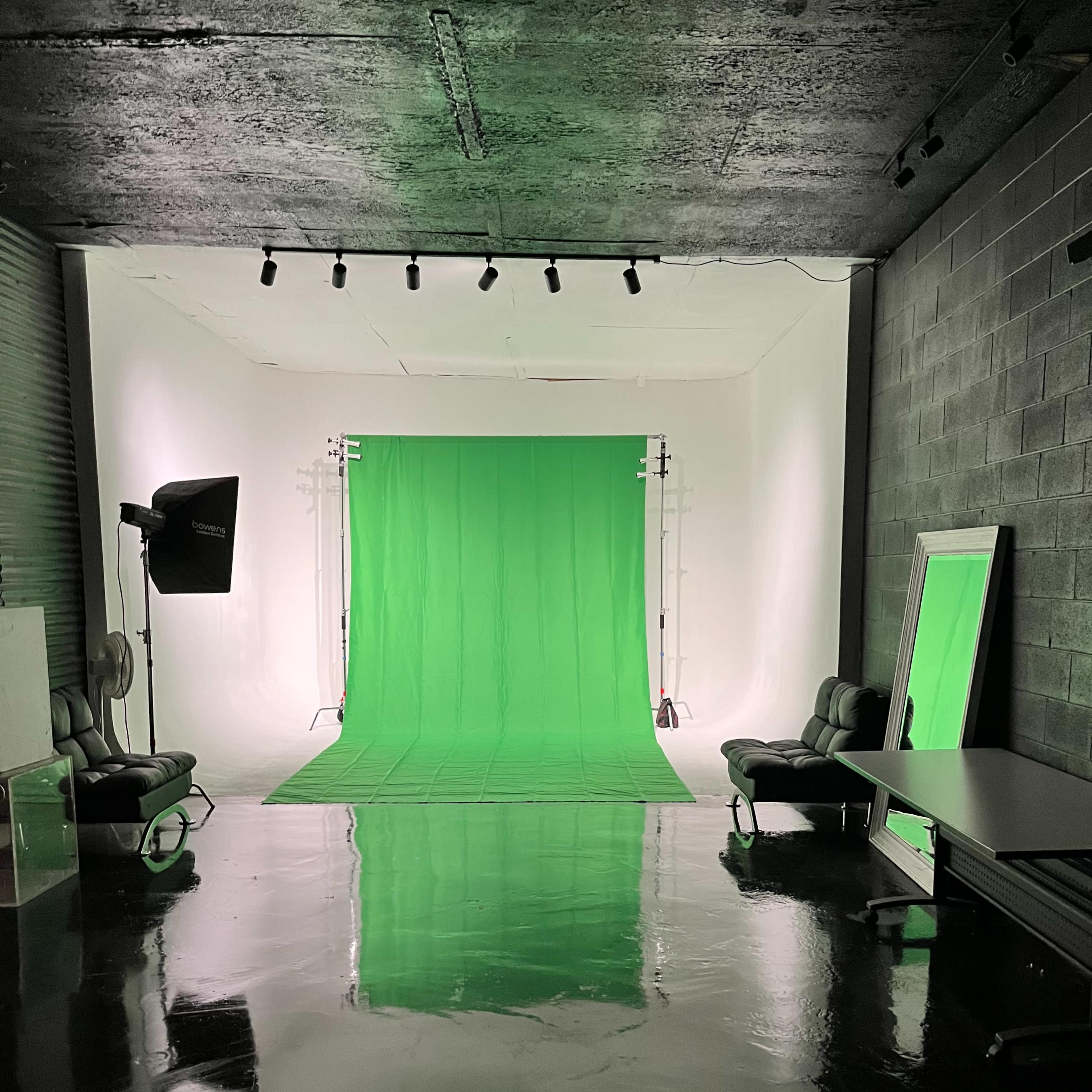 A photography studio with a green backdrop, equipped with lights, chairs, and reflective surfaces on the floor.