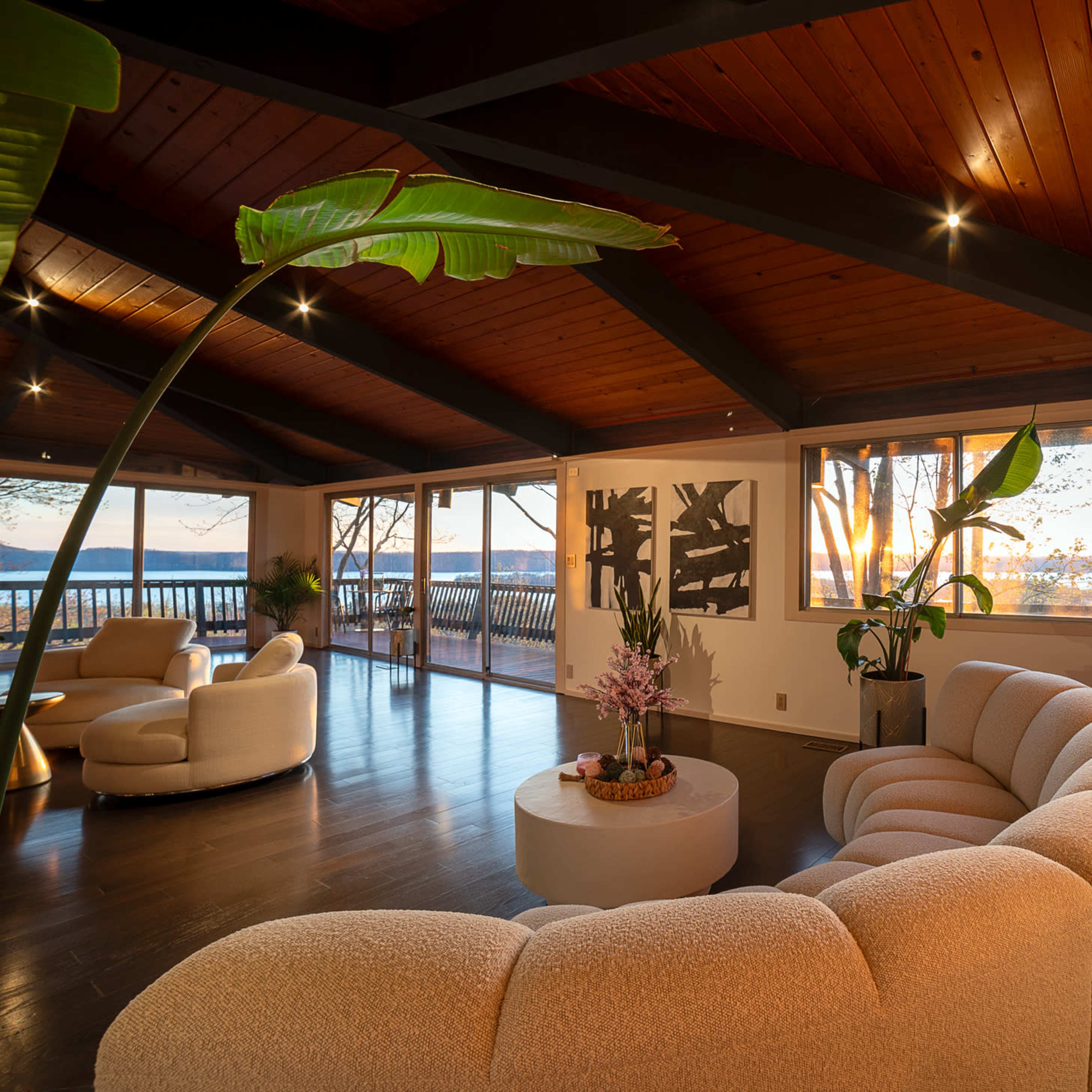 A modern living room features a curved white sofa, a round coffee table, and large windows overlooking a scenic view.
