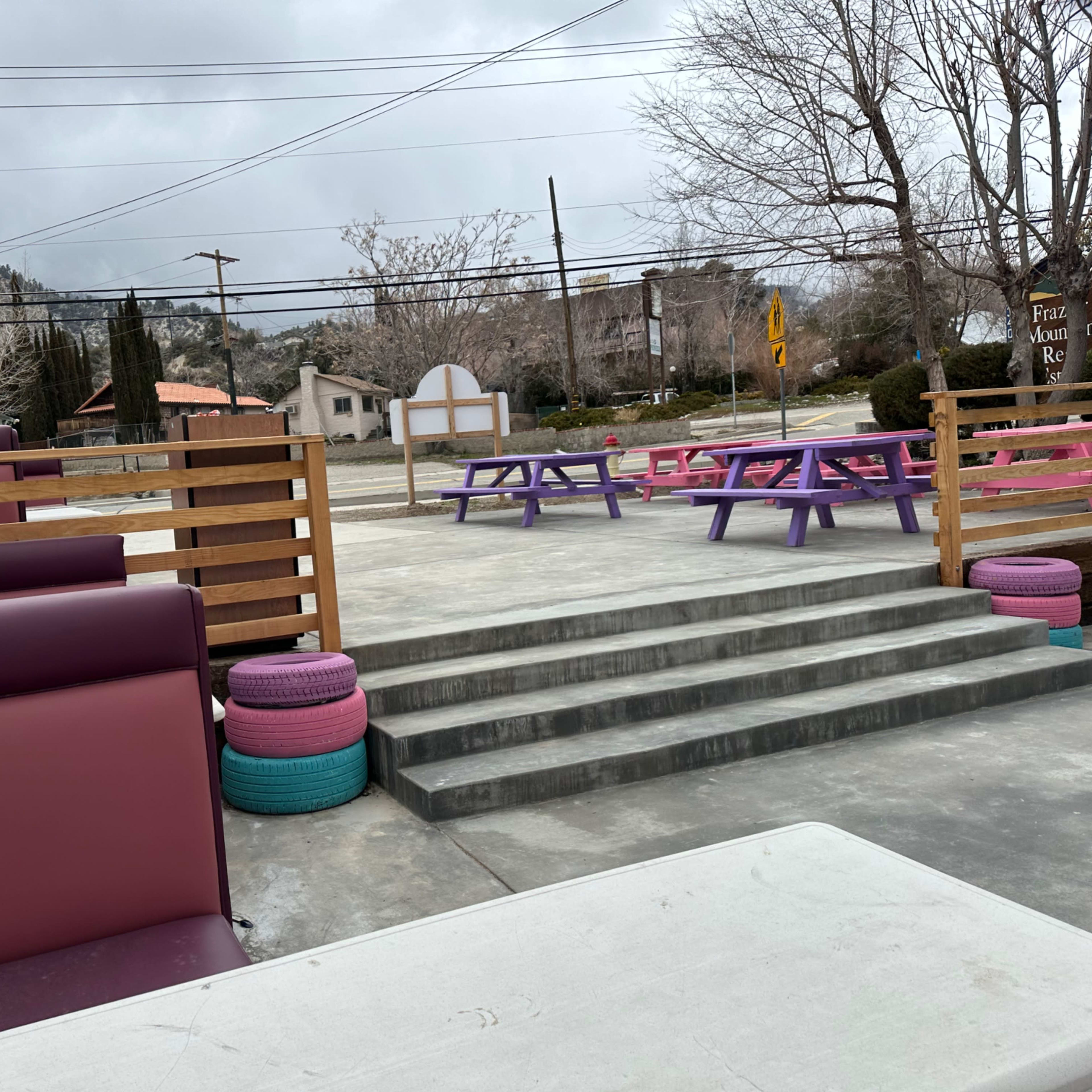 An outdoor seating area with colorful benches and tables, surrounded by a gray sky and sparse trees.