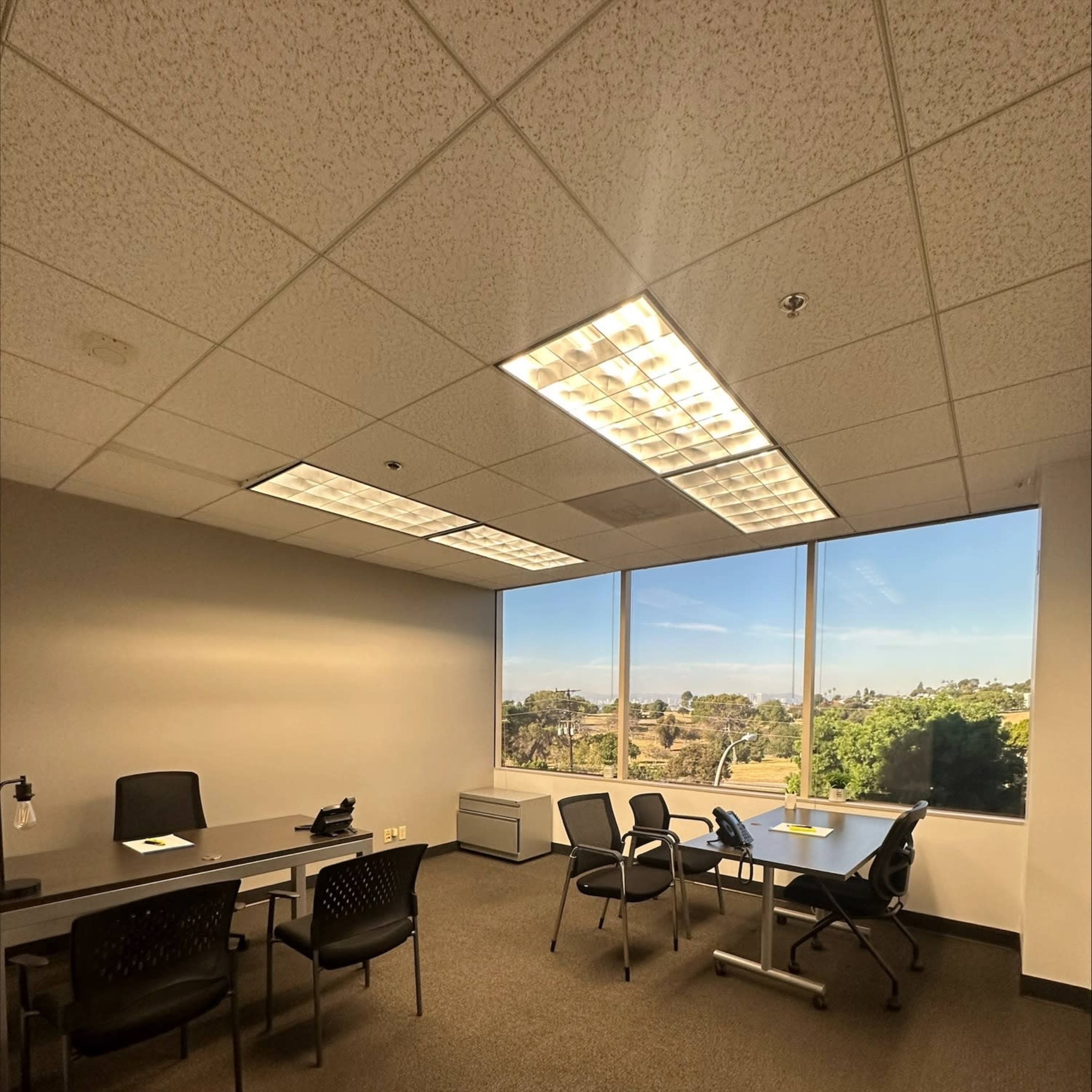 An empty office space features a large window with a view and several chairs arranged around a table.