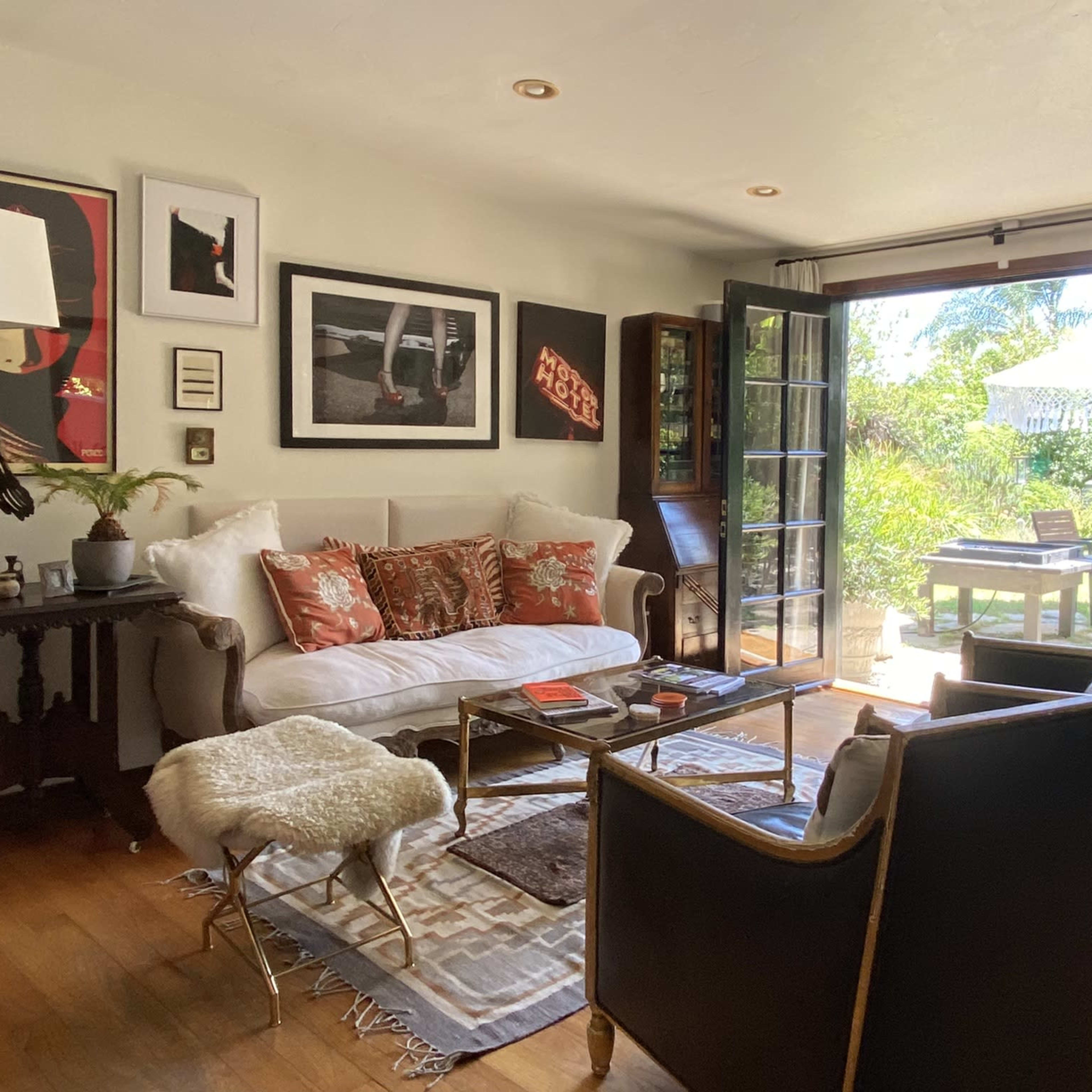 A living room with a white sofa, two dark armchairs, a glass coffee table, and large doors leading to a garden area.