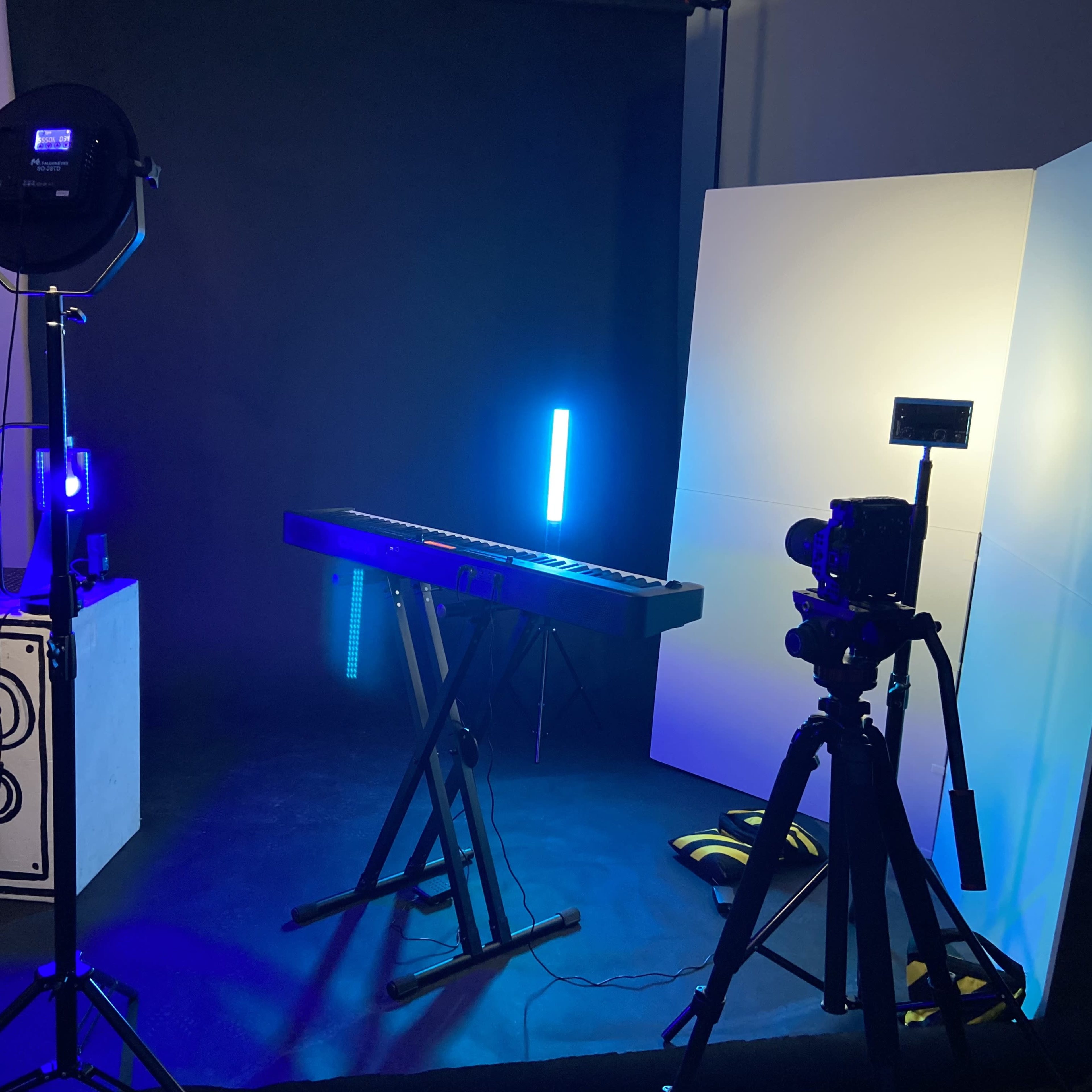 A music keyboard setup with a camera on a tripod and various lighting elements in a studio environment.