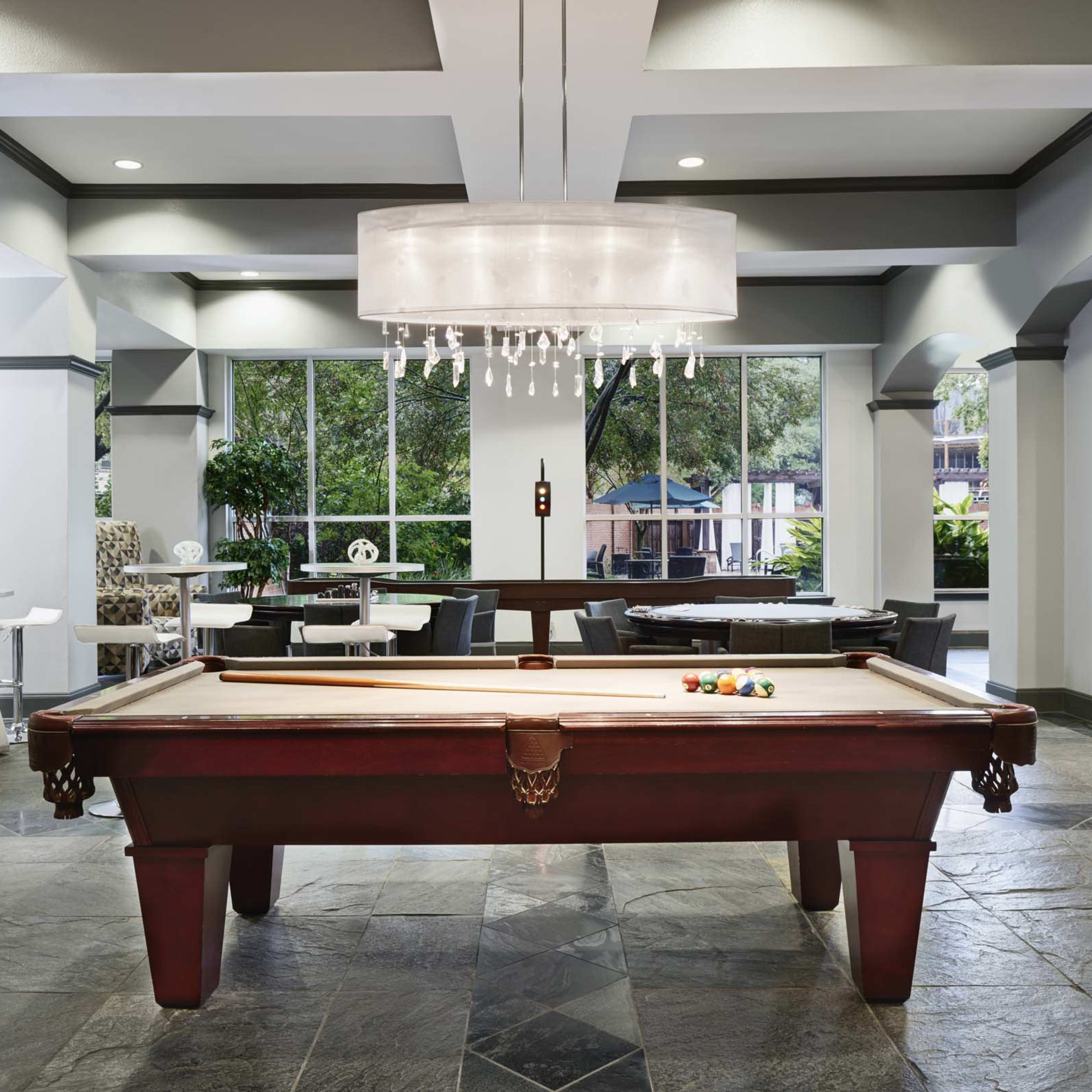 A spacious lounge area featuring a billiards table in the center, surrounded by modern seating and large windows letting in natural light.