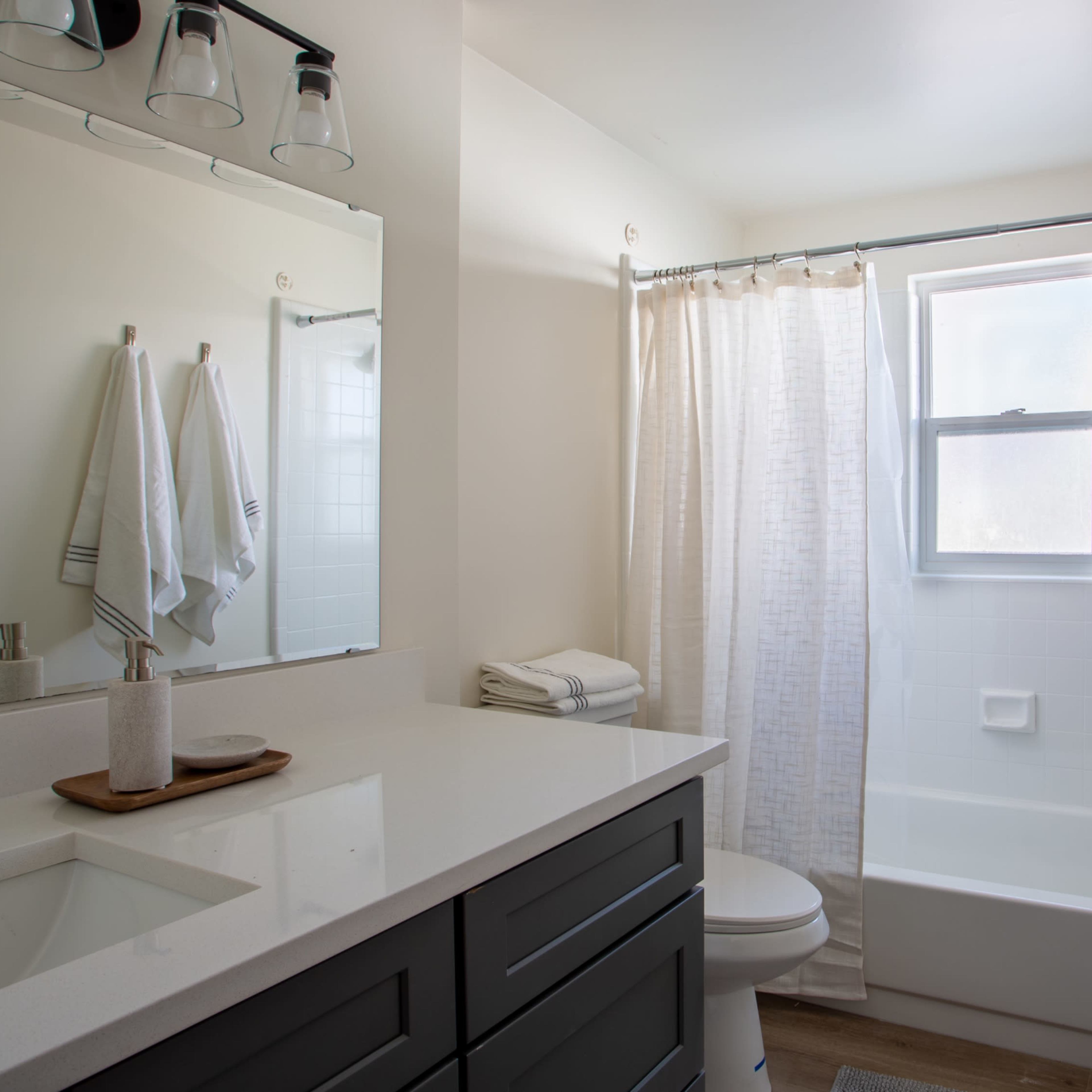 A modern bathroom featuring a white bathtub, a wall-mounted mirror, and a grey vanity with a sink.