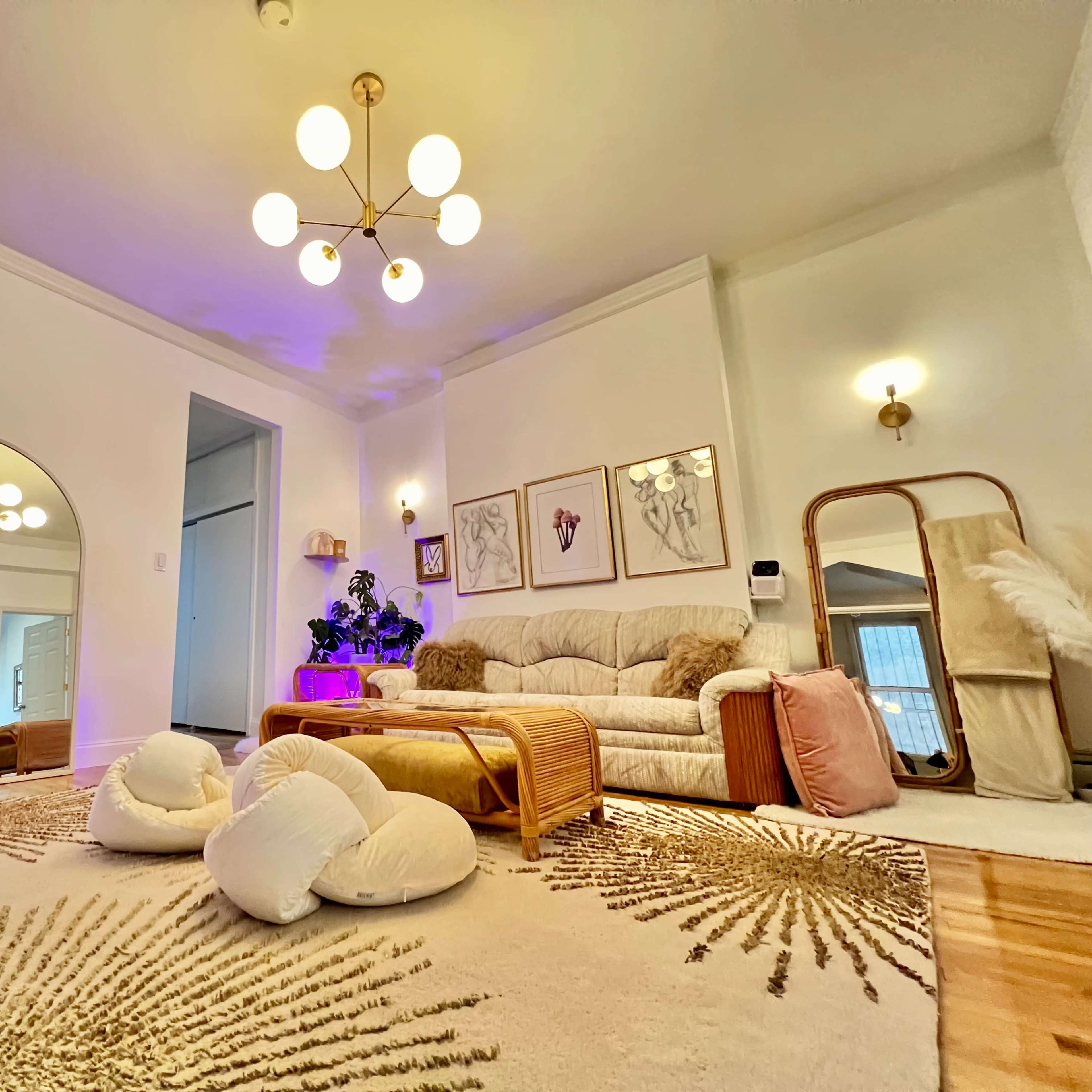 A well-decorated living room features a large beige sofa, a round mirror, and a decorative rug with gold patterns, illuminated by a modern light fixture.