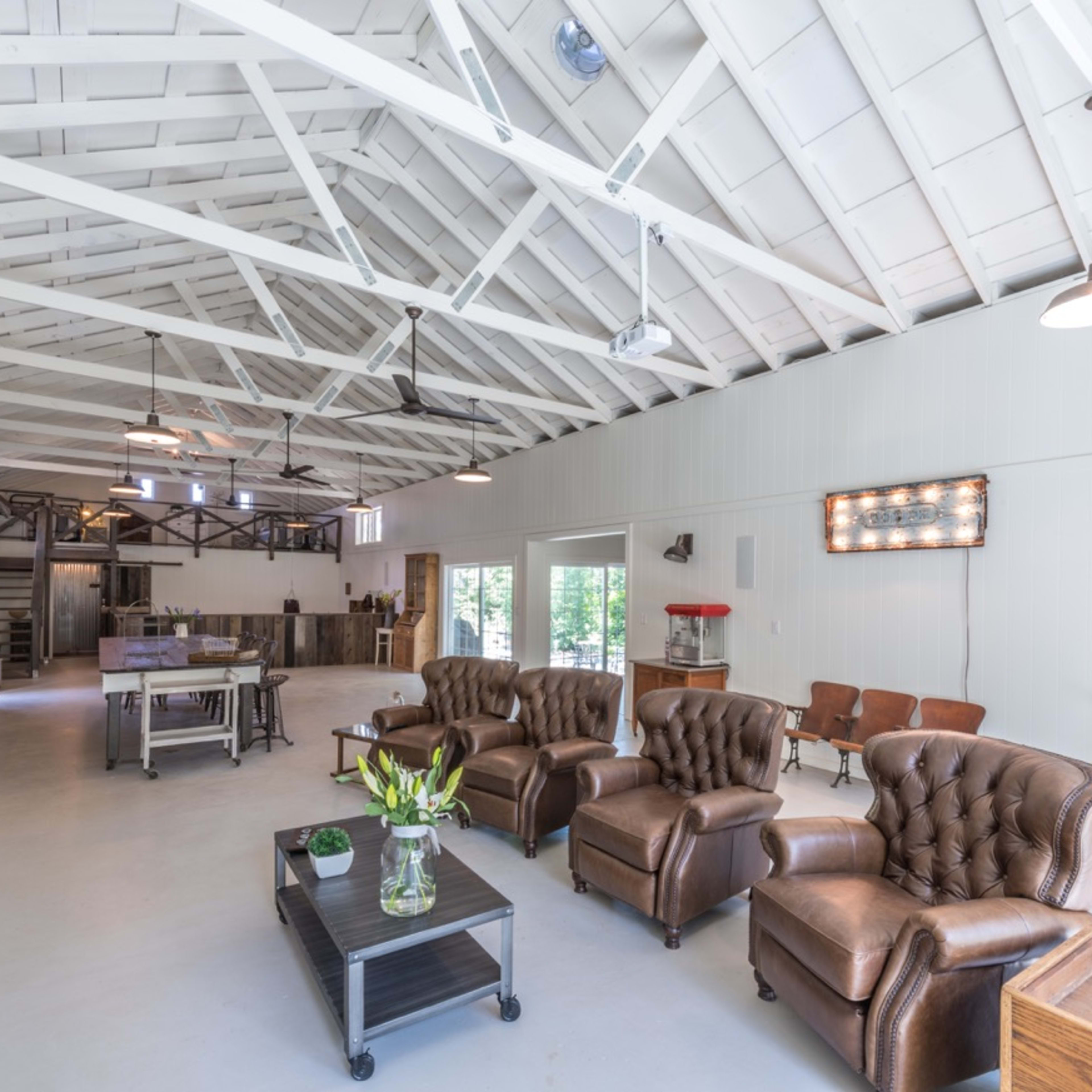 A spacious room with high ceilings, featuring brown leather sofas, a coffee table, a dining area, and industrial-style decor.