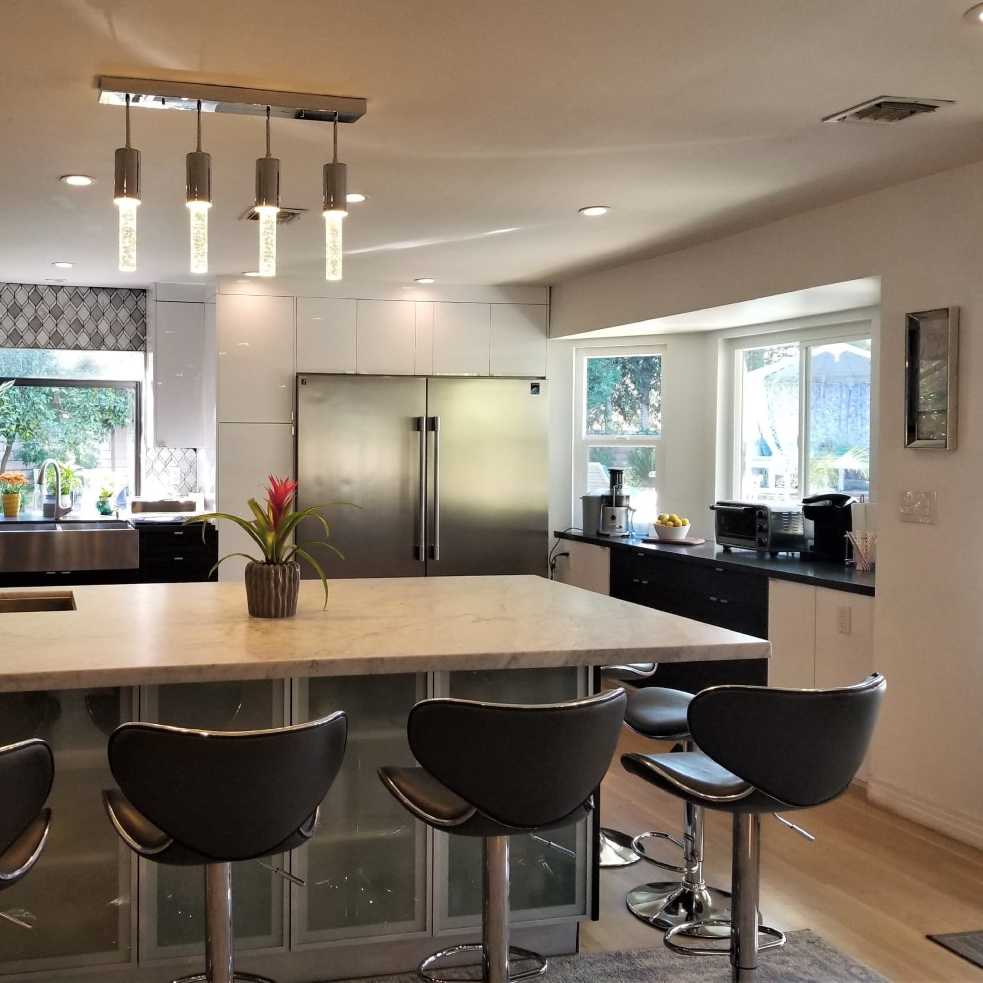 A modern kitchen features a large island with bar stools, stainless steel appliances, and a mix of dark and light cabinetry.