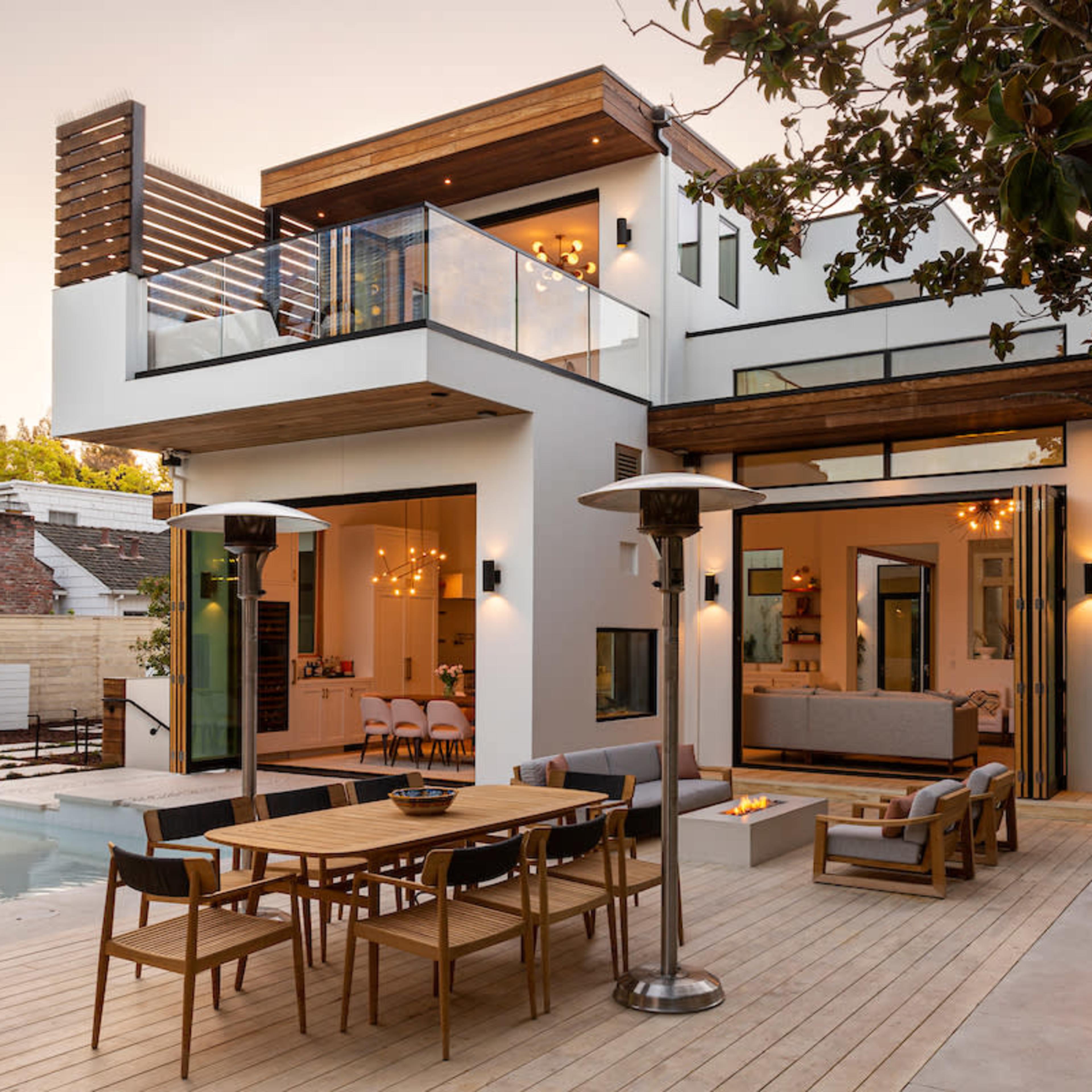 A modern two-story house features a spacious outdoor deck with a dining area, a pool, and large glass doors that connect to an interior living space.