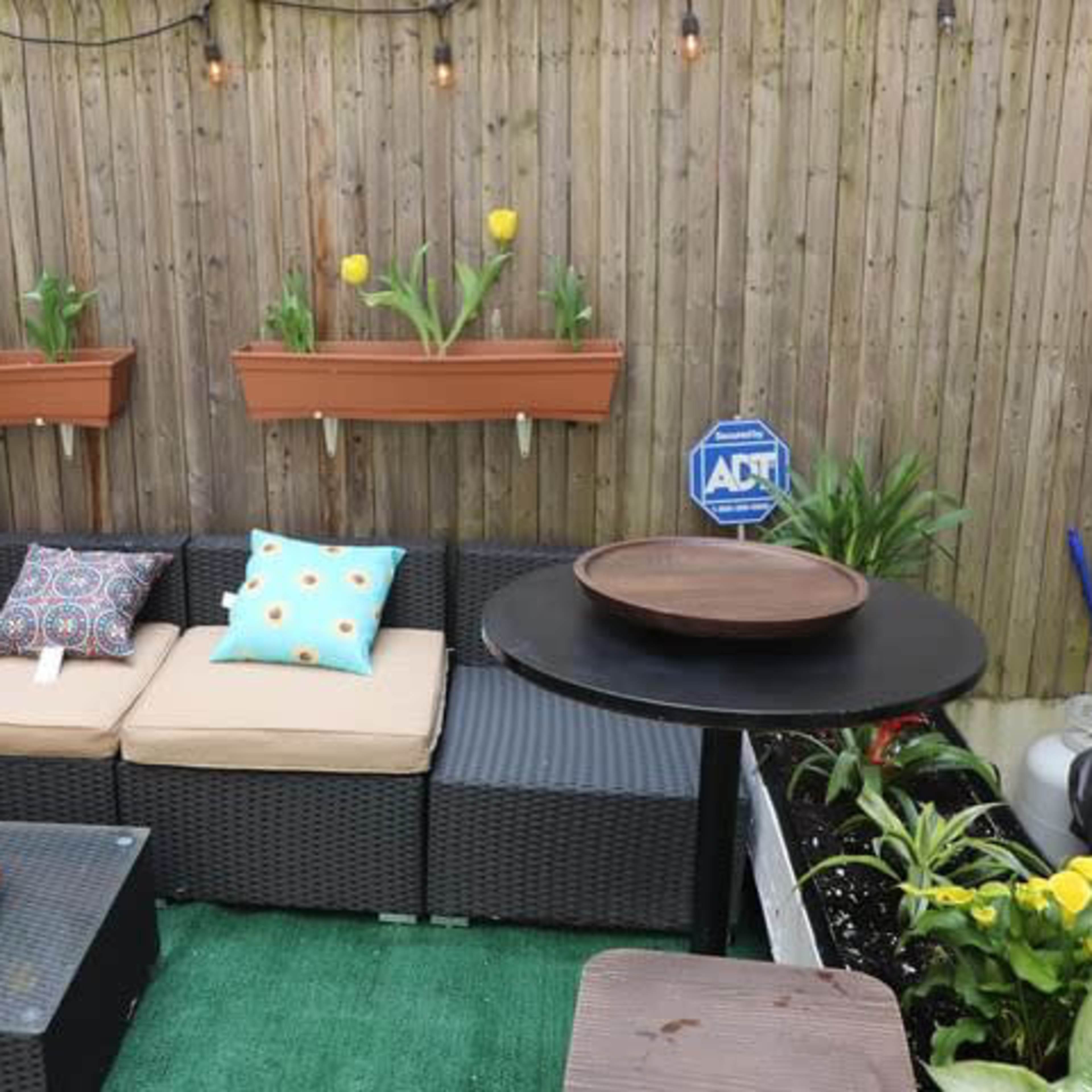 A patio area with dark wicker furniture, colorful cushions, potted tulips on the wall, and a table on a green grass-like surface.