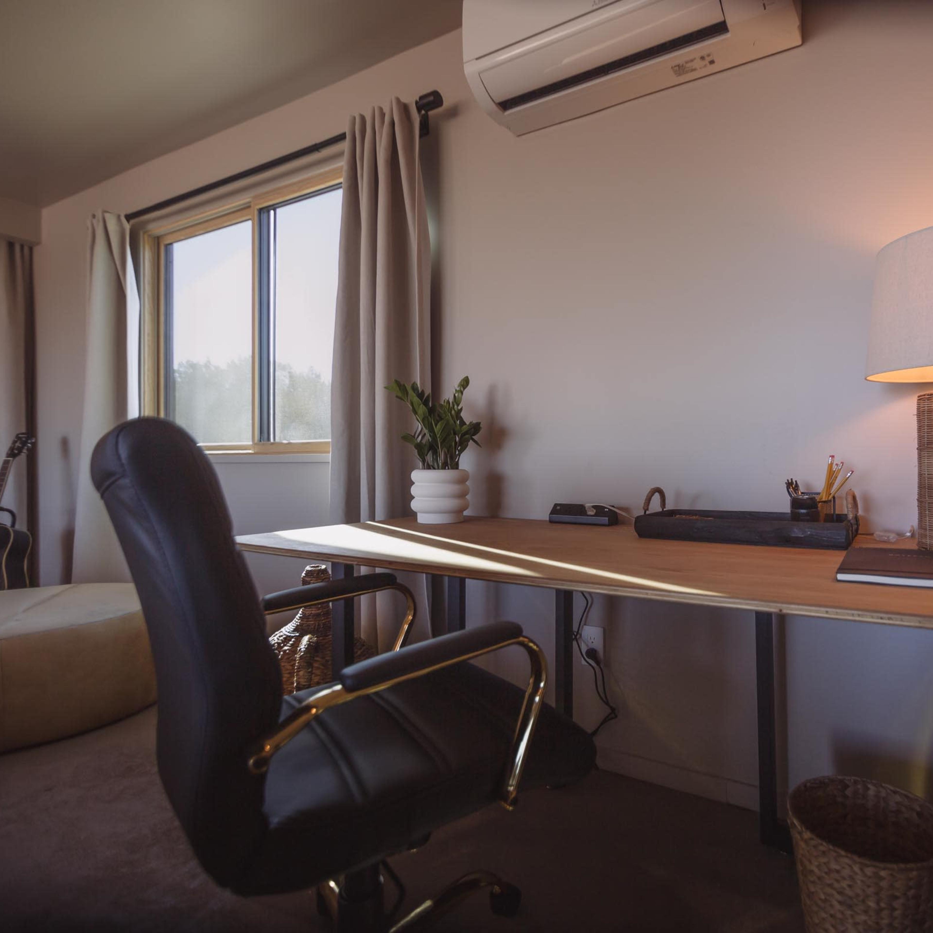 A workspace features a wooden desk with a lamp, a potted plant, and a chair, situated beside a window with curtains.