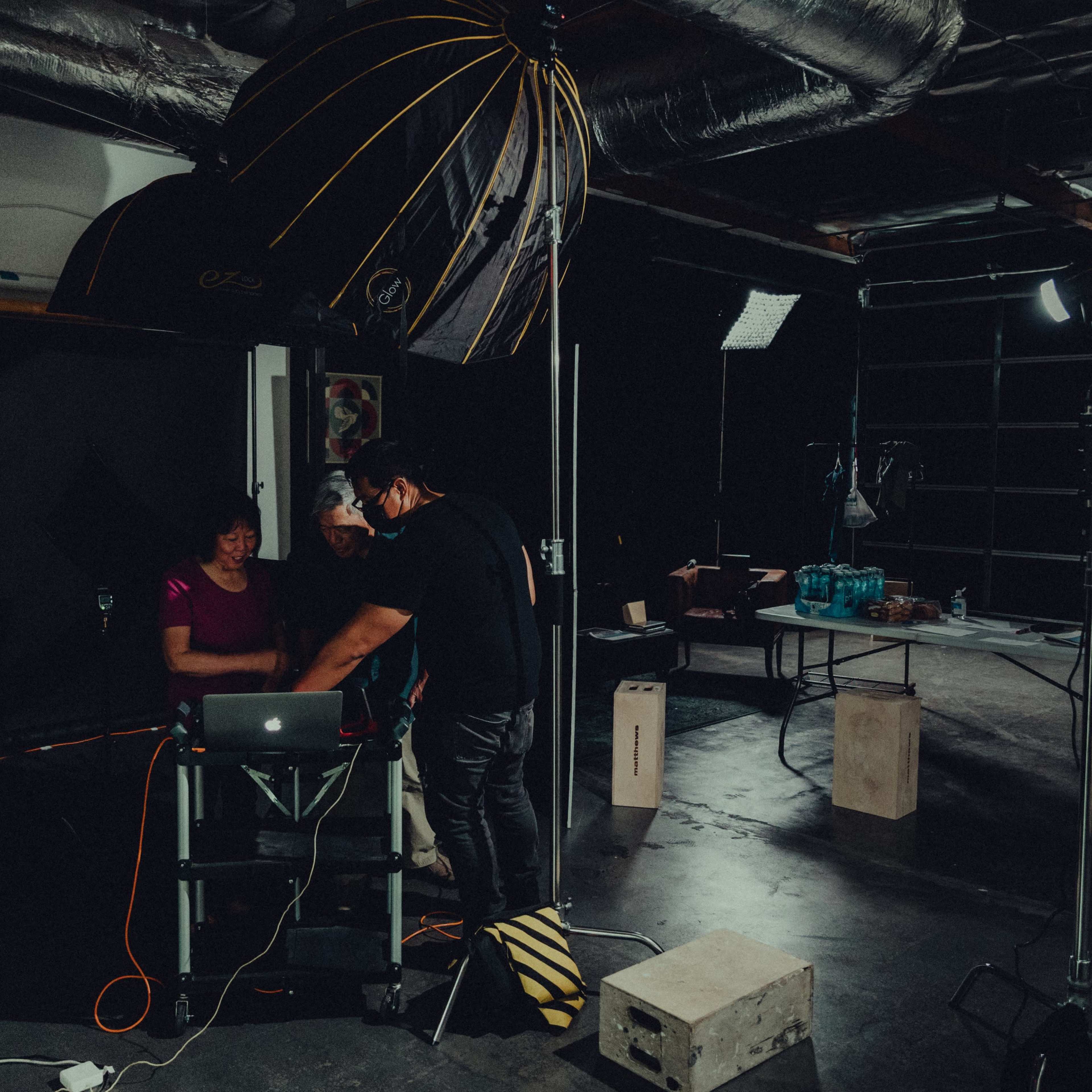 Two individuals are collaborating at a laptop in a photography studio equipped with lighting and backdrop setups.
