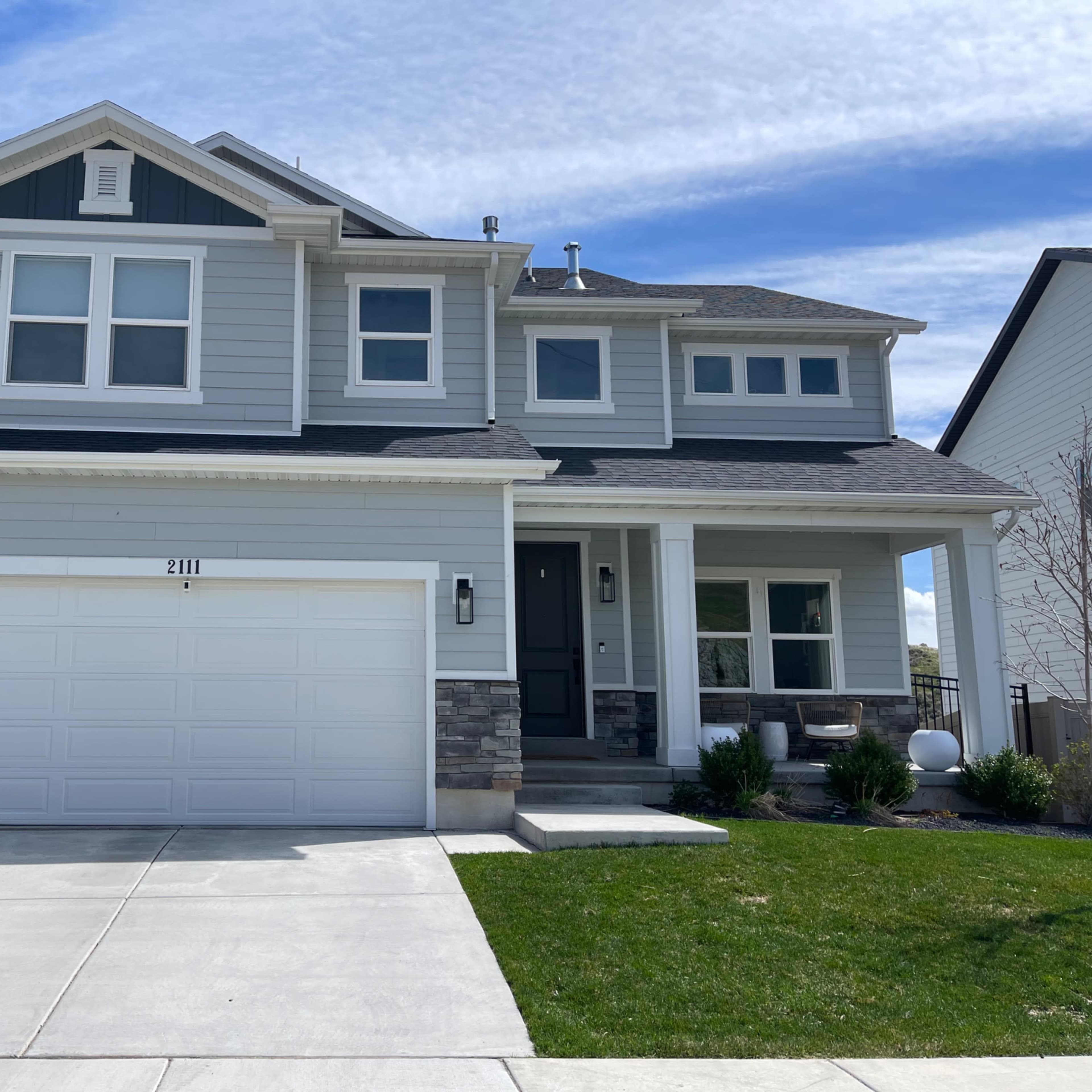 A two-story gray house with a stone-accented garage, a front porch, and a well-maintained lawn.