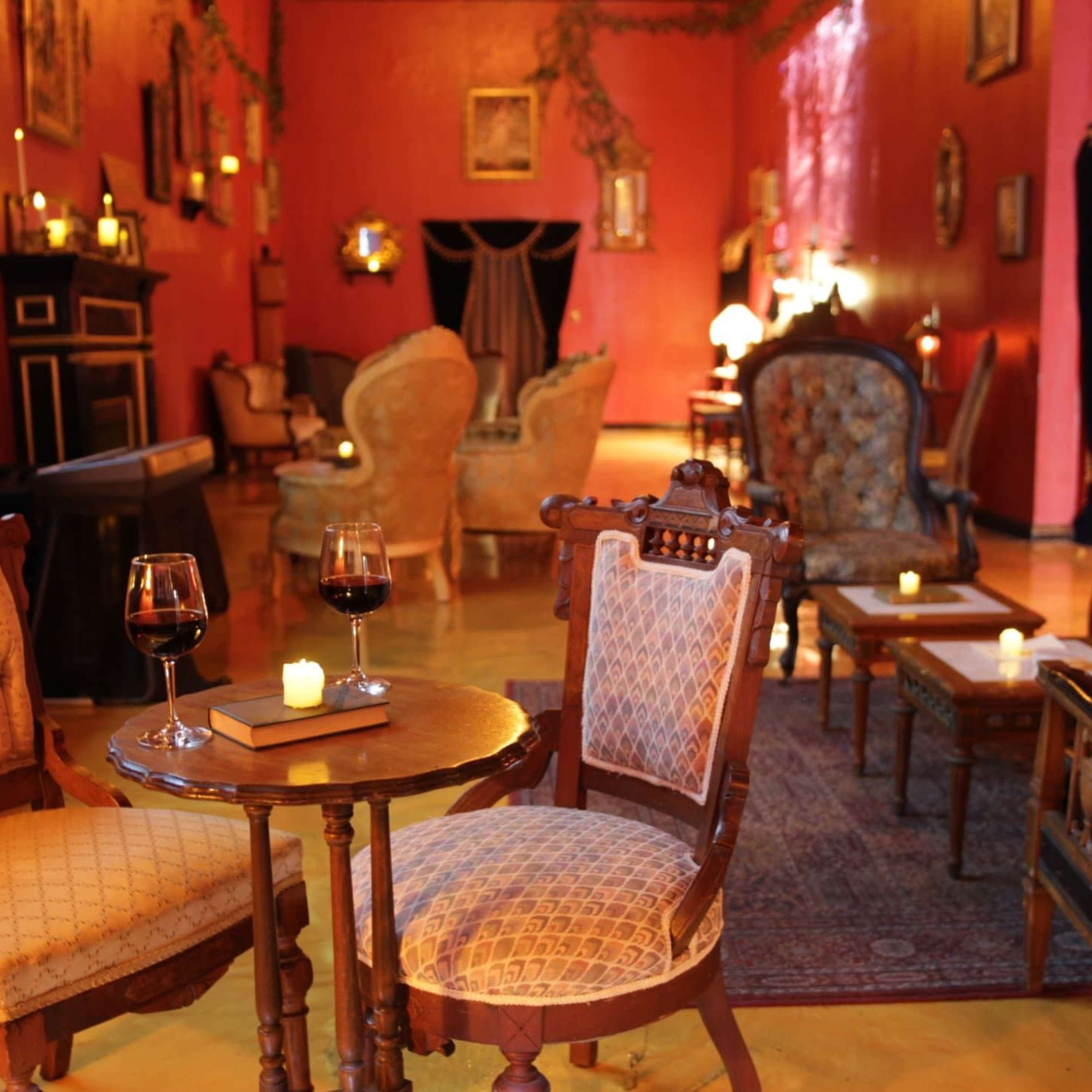 The scene depicts a cozy interior of a vintage-style lounge with vintage furniture, dim lighting, and two glasses of red wine on a small table.