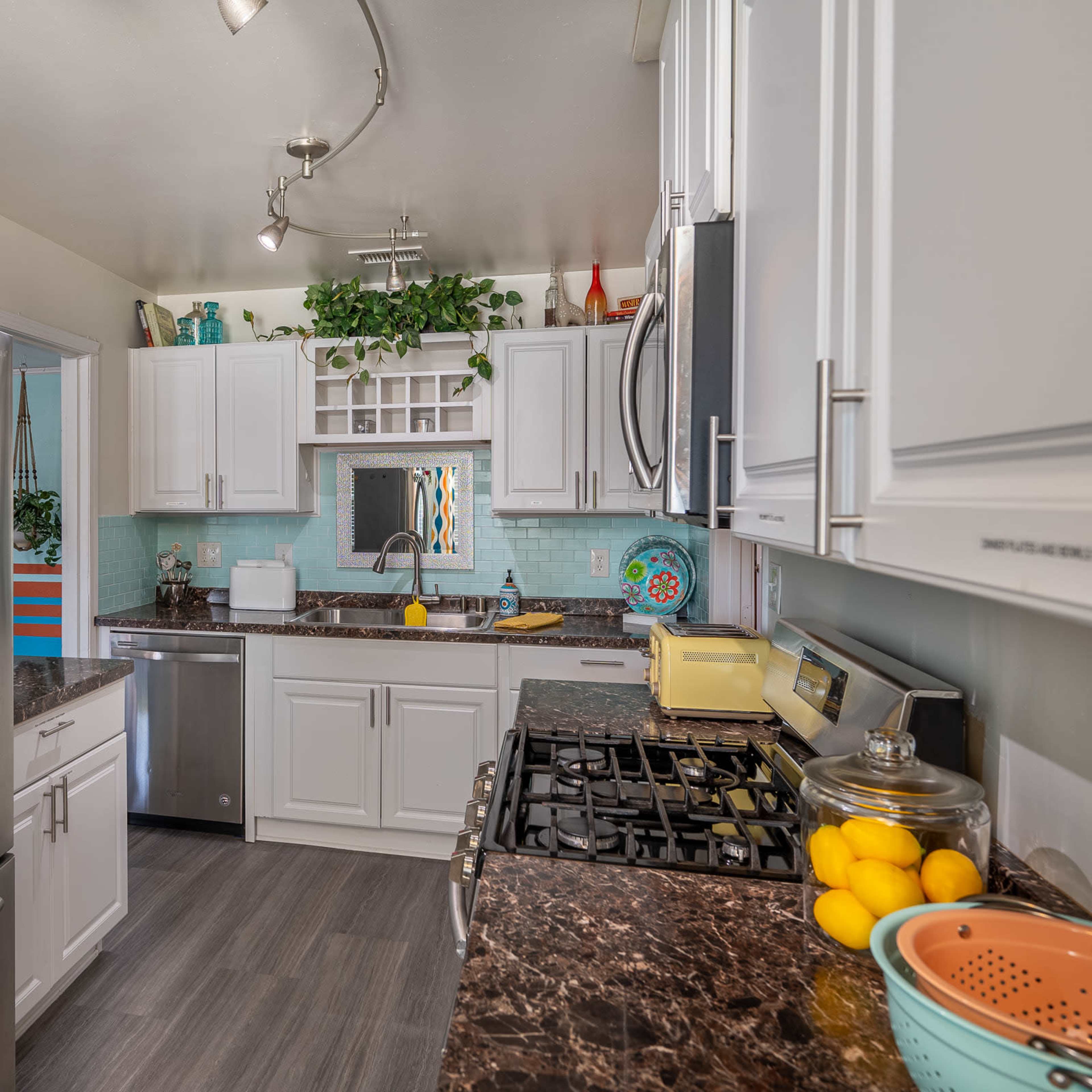 A modern kitchen features stainless steel appliances, white cabinetry, and a colorful backsplash with decorative plants.