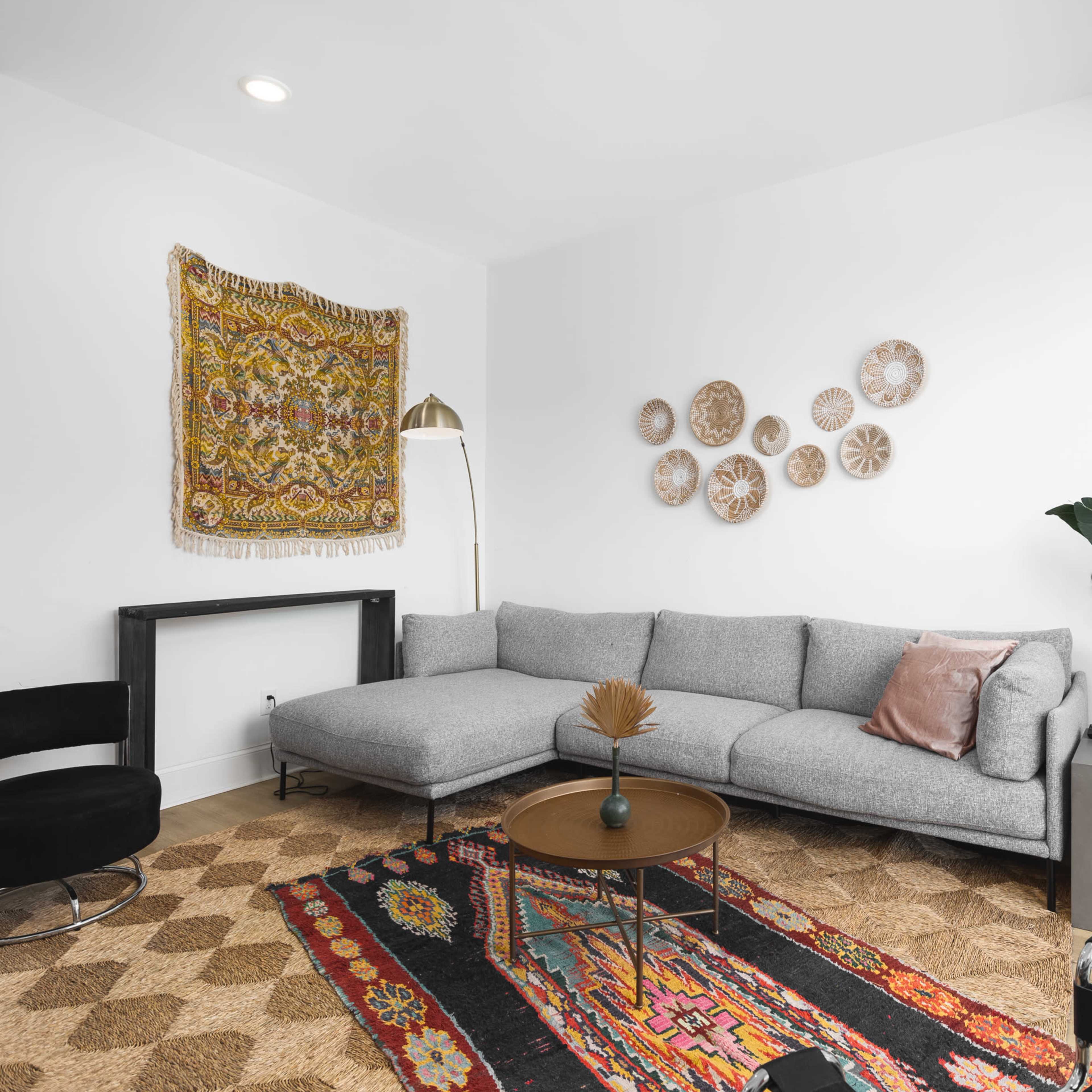 A modern living room featuring a gray sectional sofa, a round coffee table, decorative wall art, and lush indoor plants.
