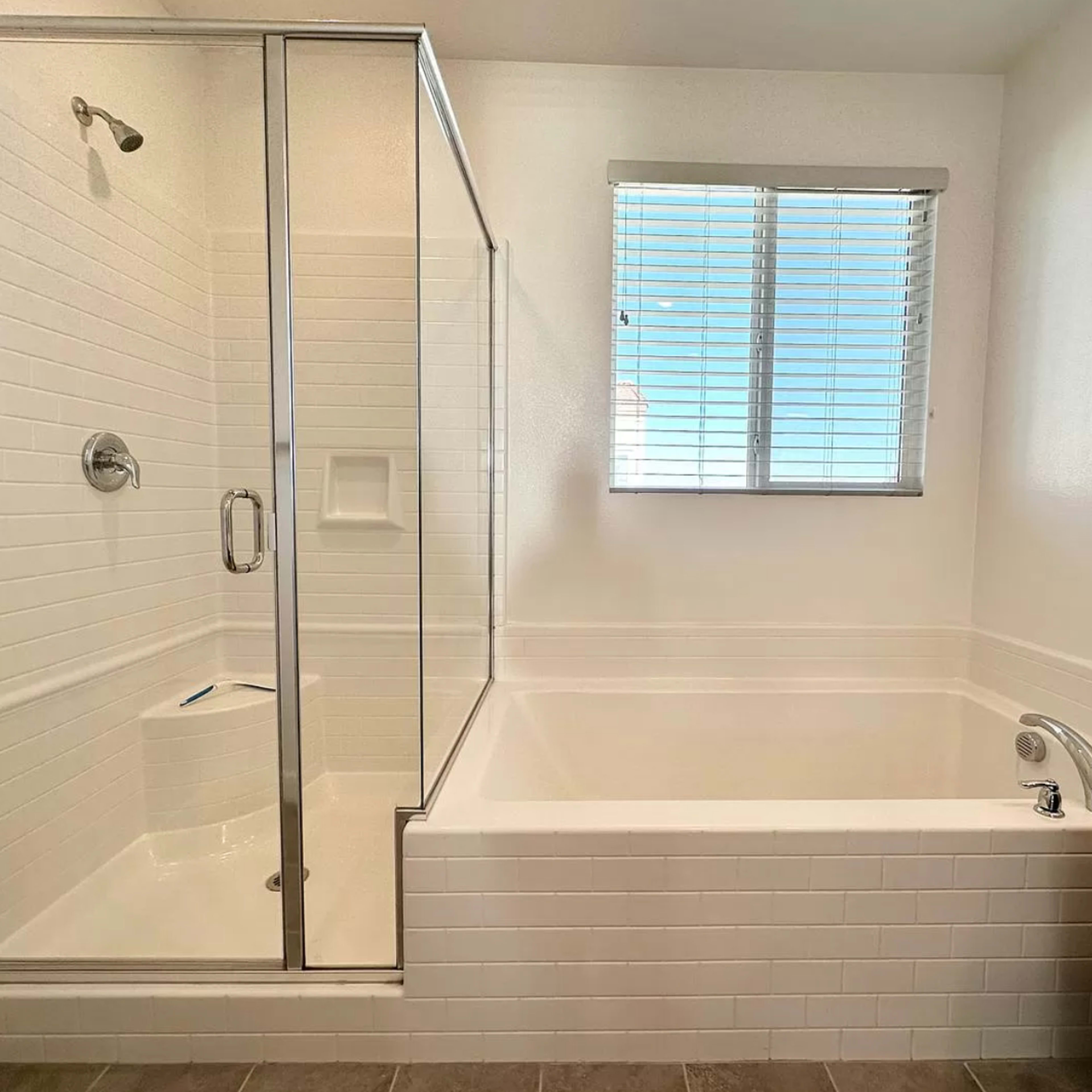 A bathroom featuring a glass-enclosed shower and a separate bathtub next to a window with blinds.