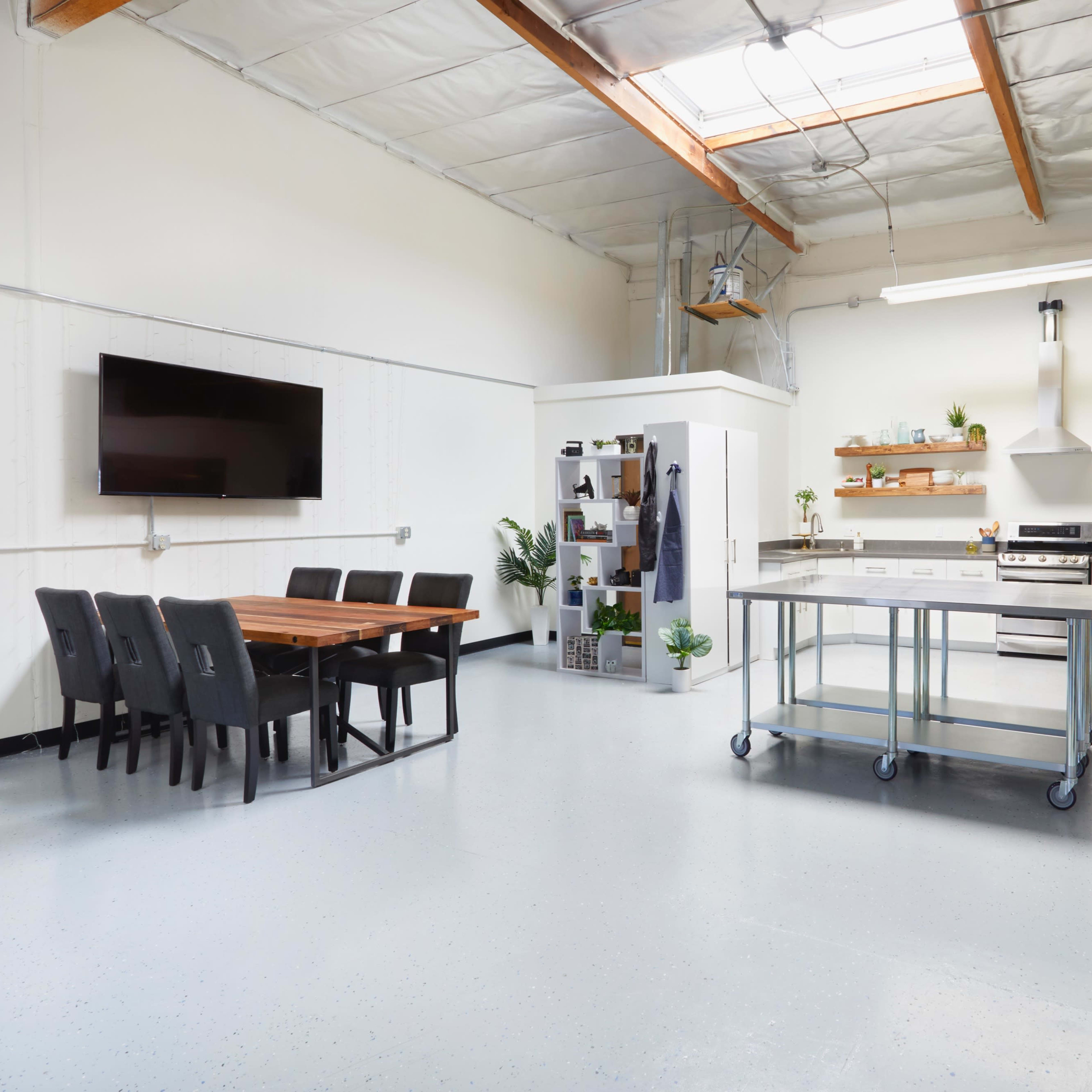 A spacious, modern kitchen with a dining area, featuring a large table, stainless steel appliances, and plants on open shelves.
